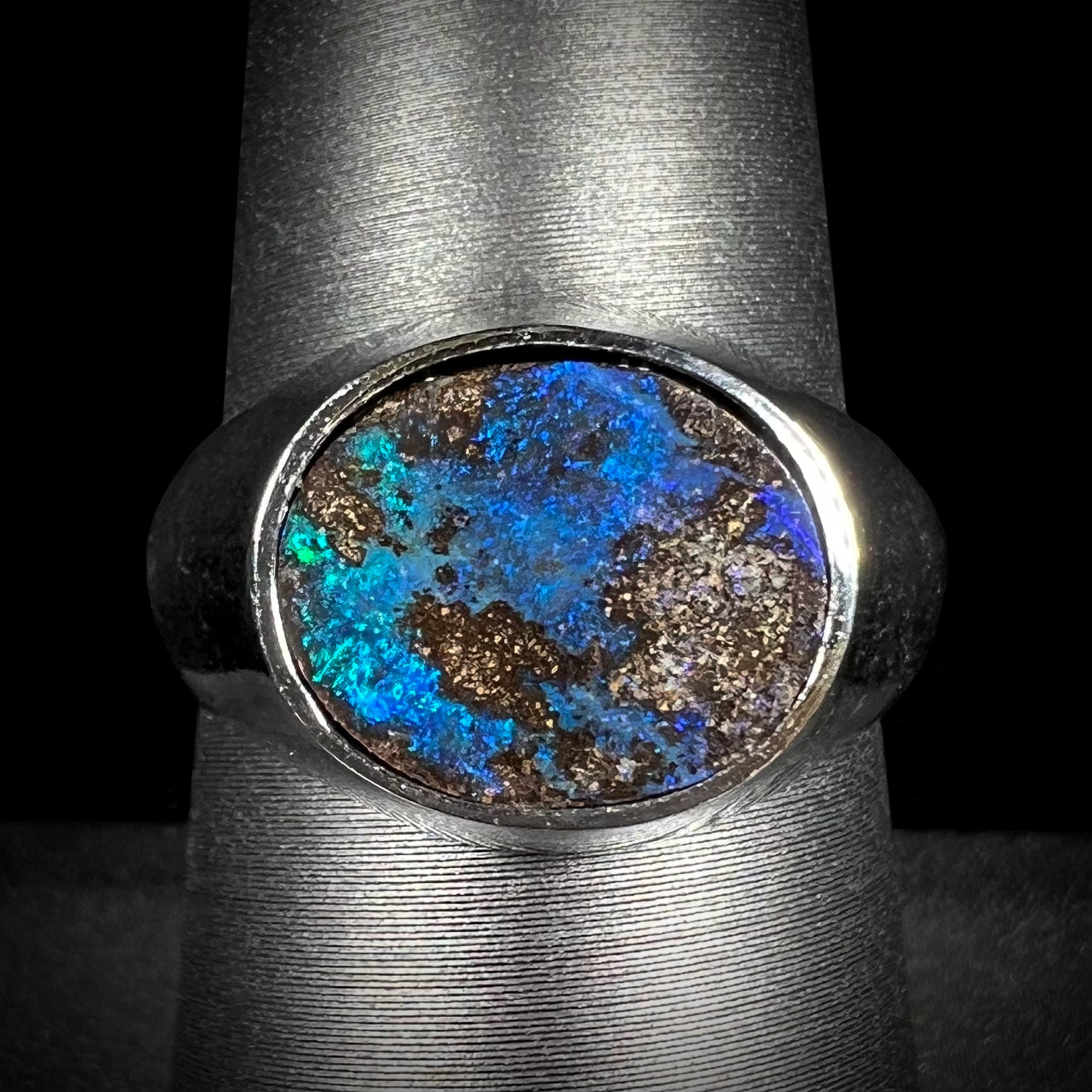A stainless steel men's Australian boulder opal ring with blue color play, shown on a ring display from the front.