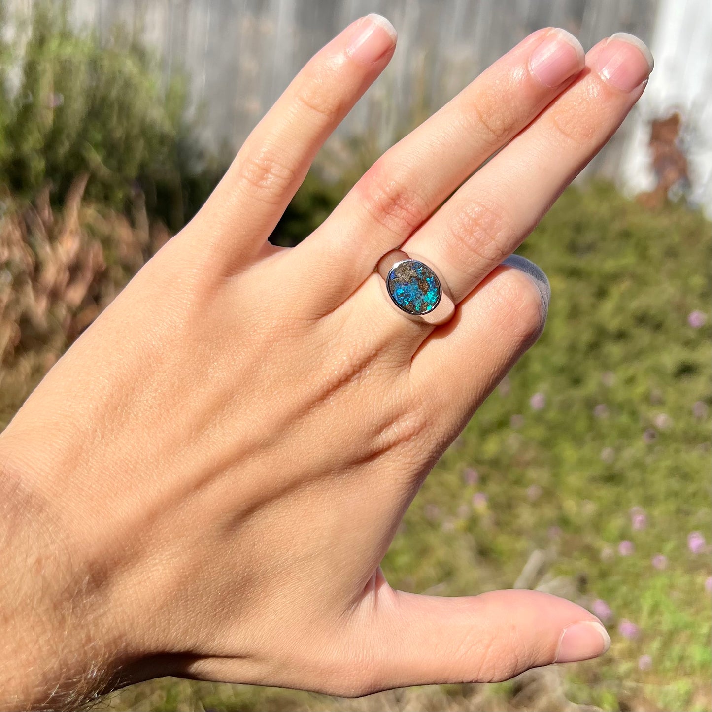 A stainless steel men's Australian boulder opal ring with blue color play, worn on a hand in sunlight.