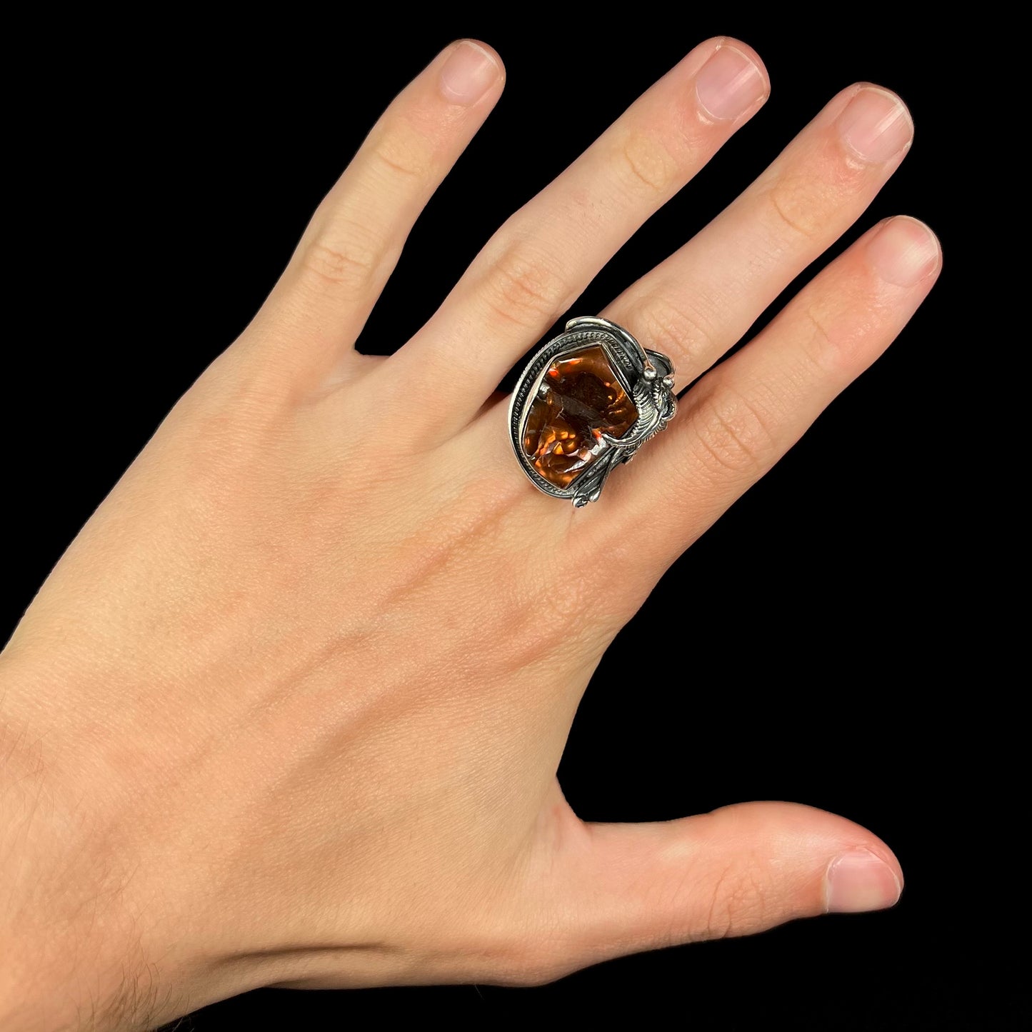A men's silver, Southwest-style fire agate ring worn on a hand against a black background.