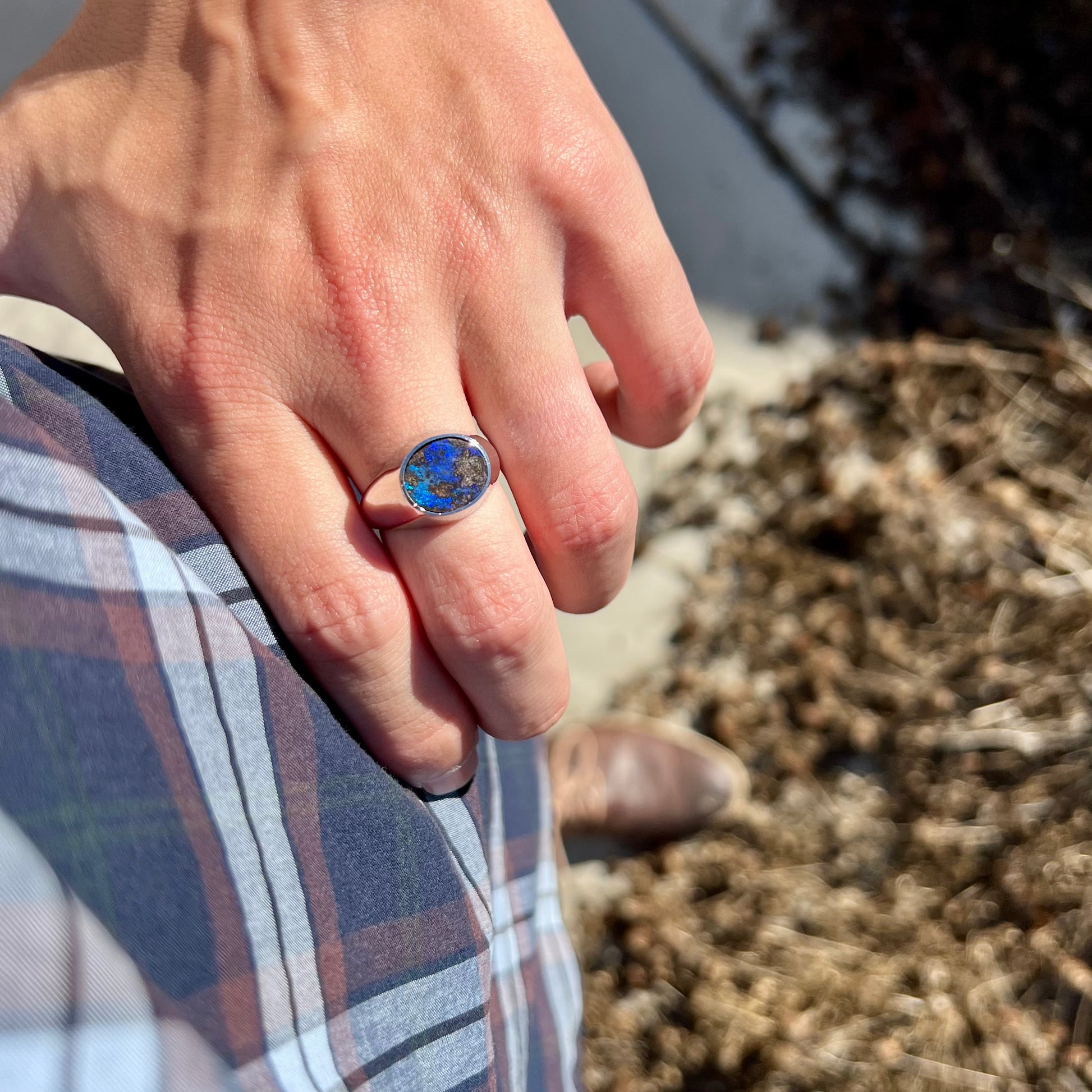 A stainless steel men's Australian boulder opal ring with blue color play worn on a hand resting on a hip.