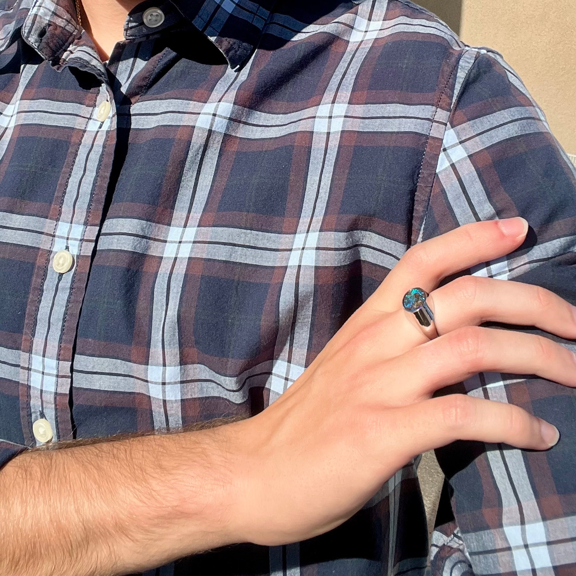 A stainless steel men's Australian boulder opal ring with blue color play worn on a hand resting on the model's shoulder.