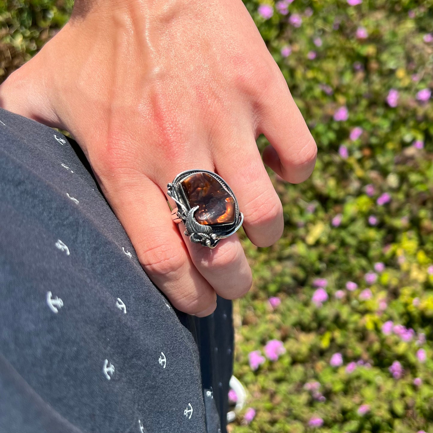 A men's silver, Southwest-style fire agate ring worn on a hand that's resting on the model's hip.