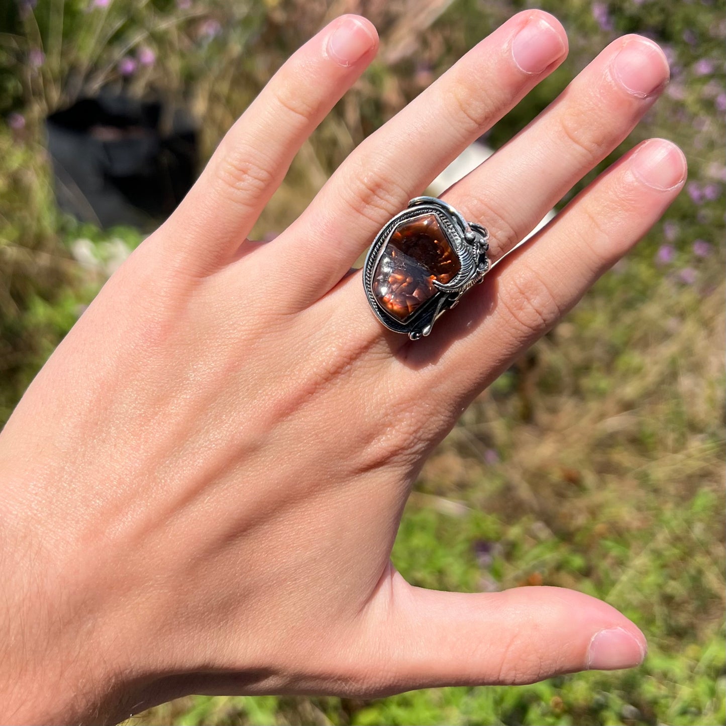 A men's silver, Southwest-style fire agate ring worn on a hand in sunlight against a blurred outdoor background.
