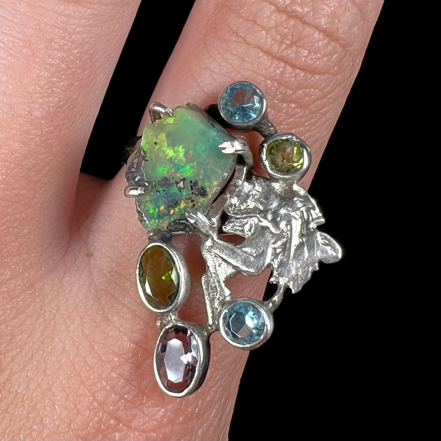 Close-up of a silver men's ring set with rough Virgin Valley opal and gems with a female figure design on a finger.