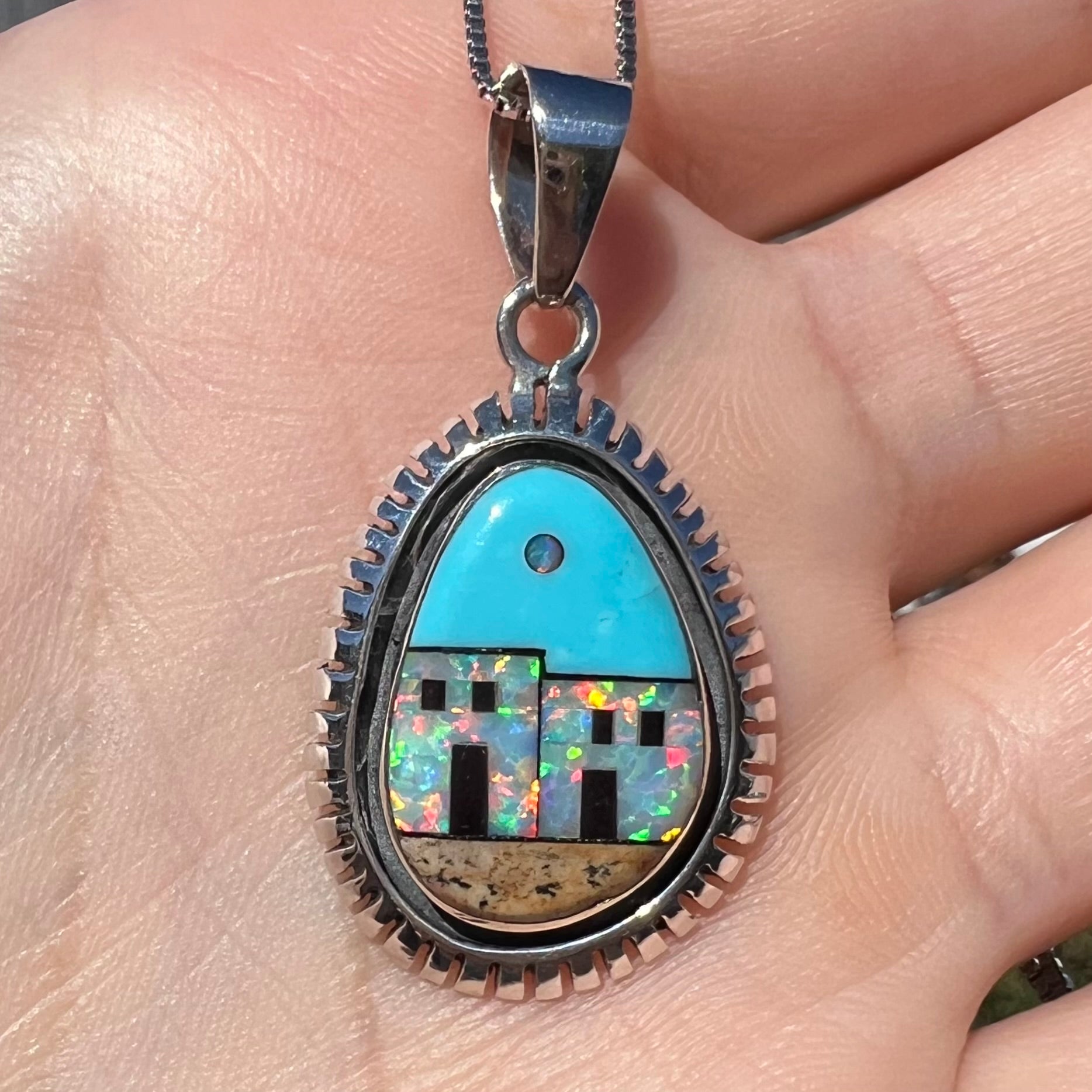 A men's Southwest-style silver opal and turquoise inlay necklace shown close-up in a hand in sunlight.