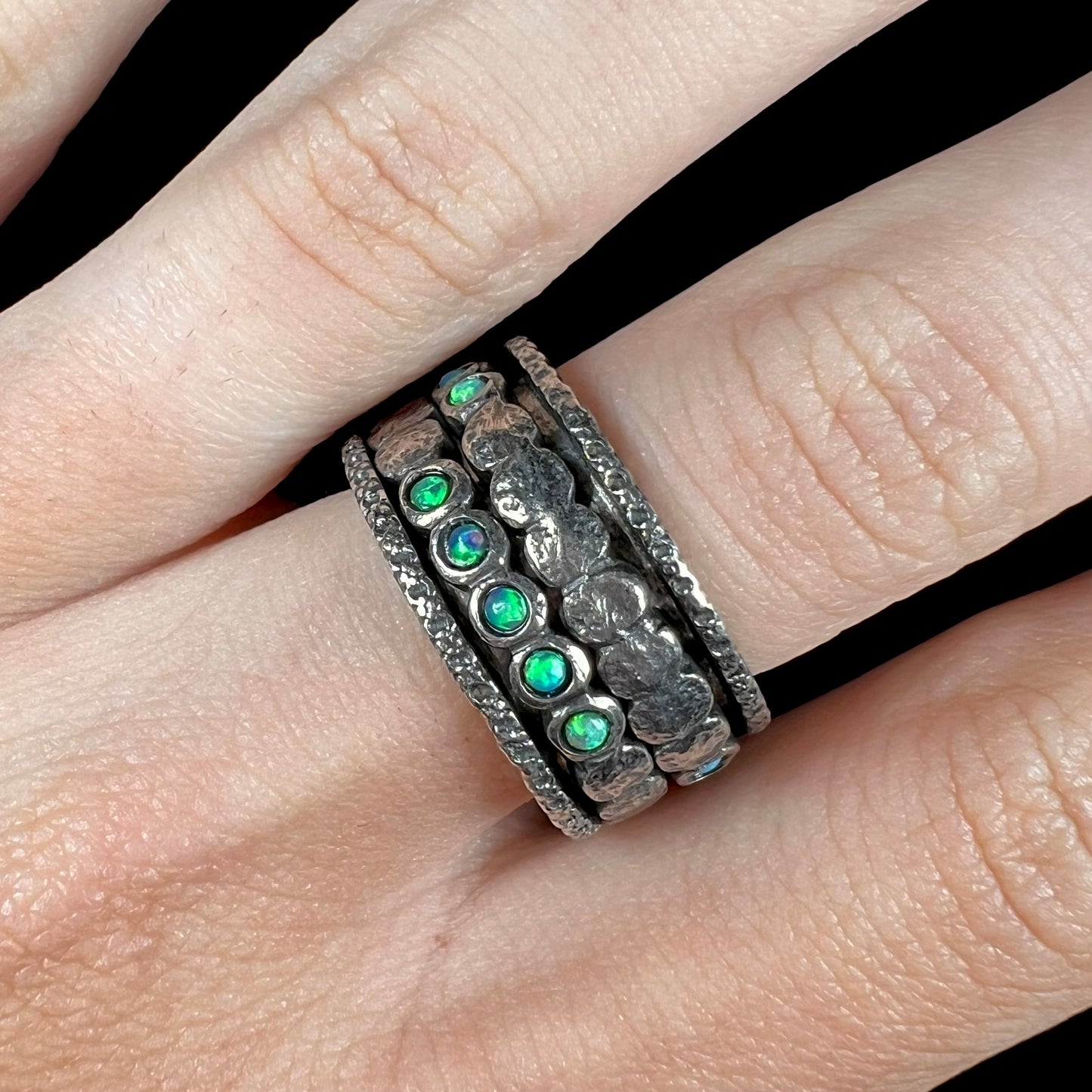 Close-up of finger wearing a men's opal ring. The opals are round with green play of color.