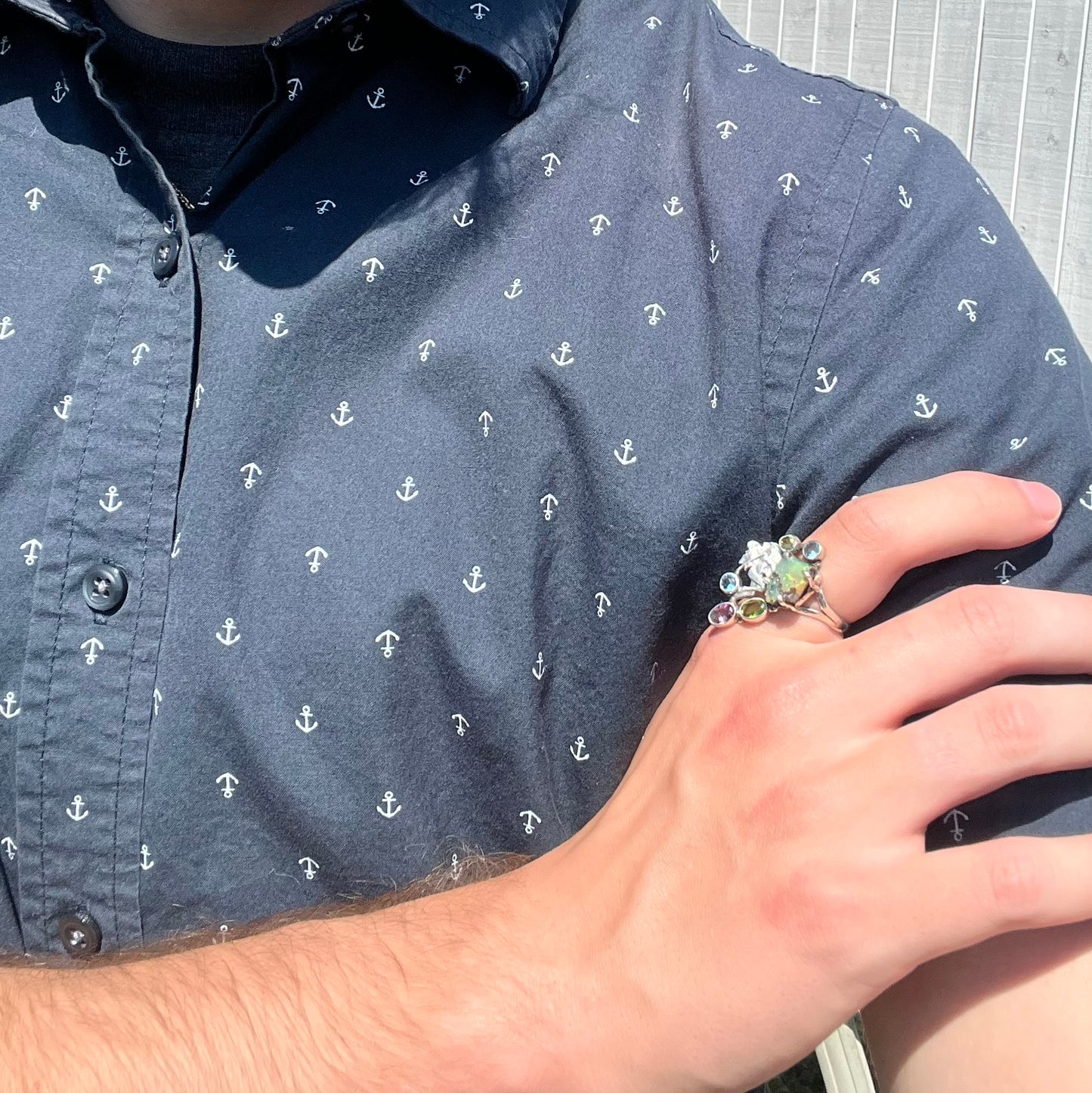 Hand wearing a handmade silver men's ring with a rough opal and gems, resting on the model's opposing shoulder.