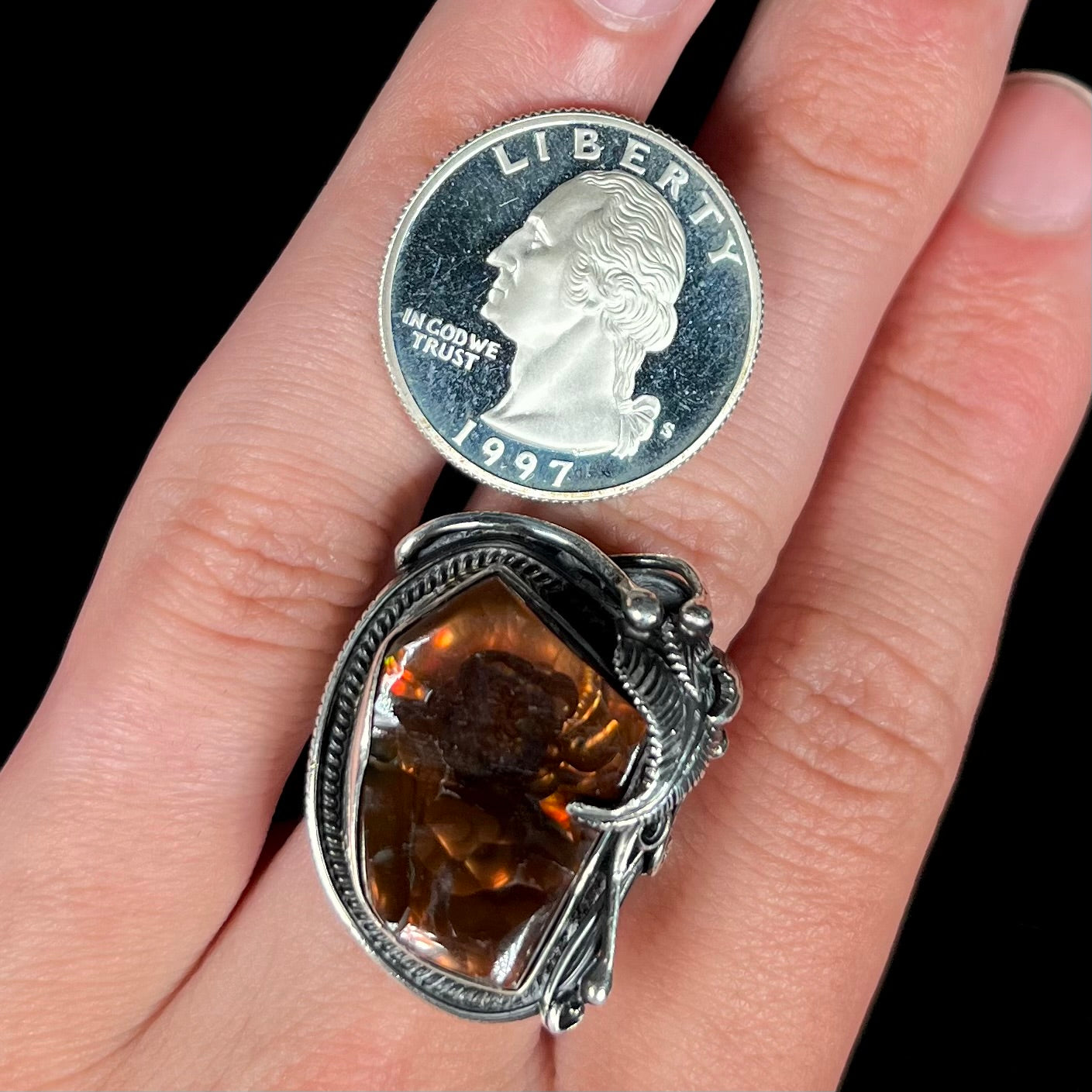 A men's silver, Southwest-style fire agate ring worn on a hand next to a 1997 S quarter coin.