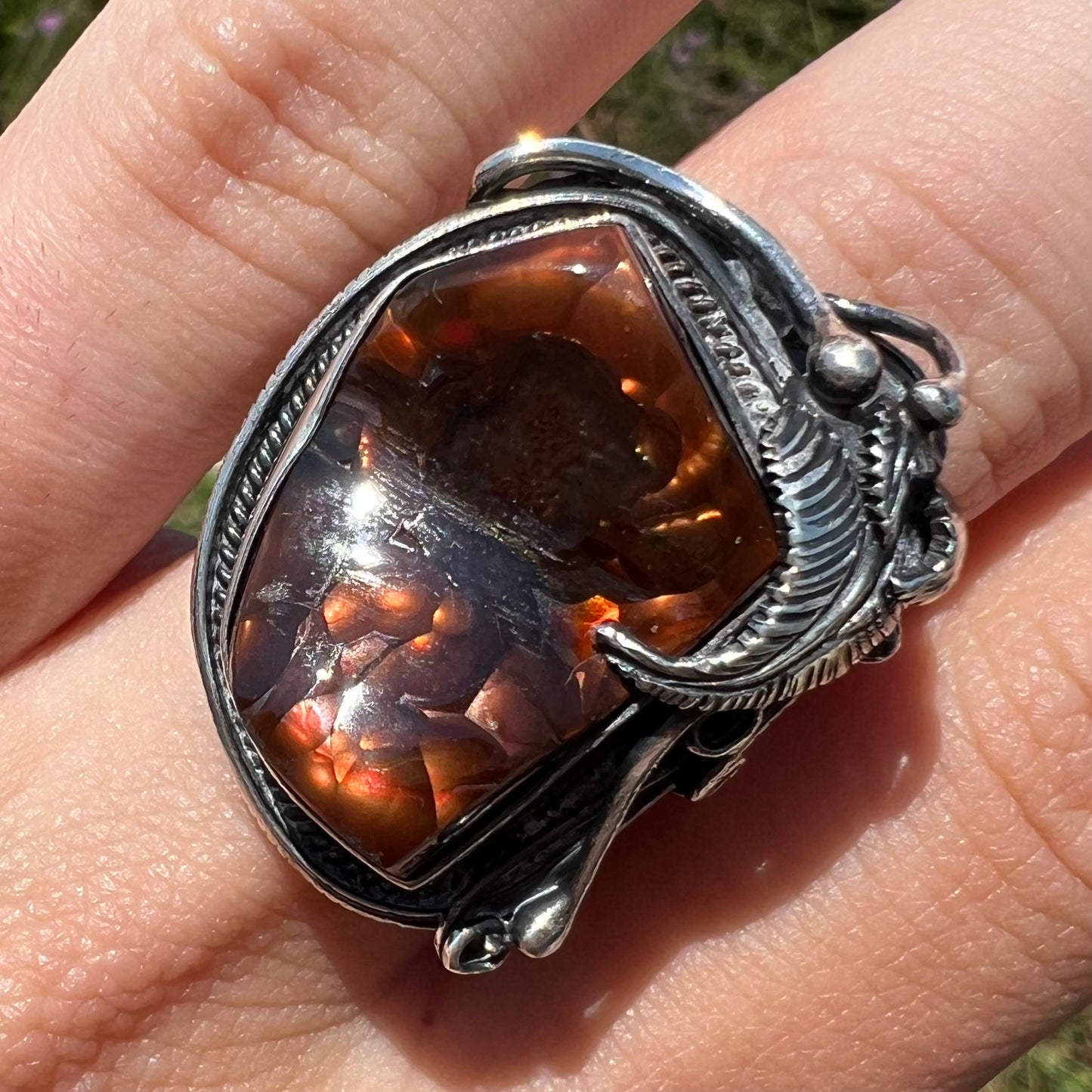 A men's silver, Southwest-style fire agate ring shown close-up in the sunlight, worn on a finger.