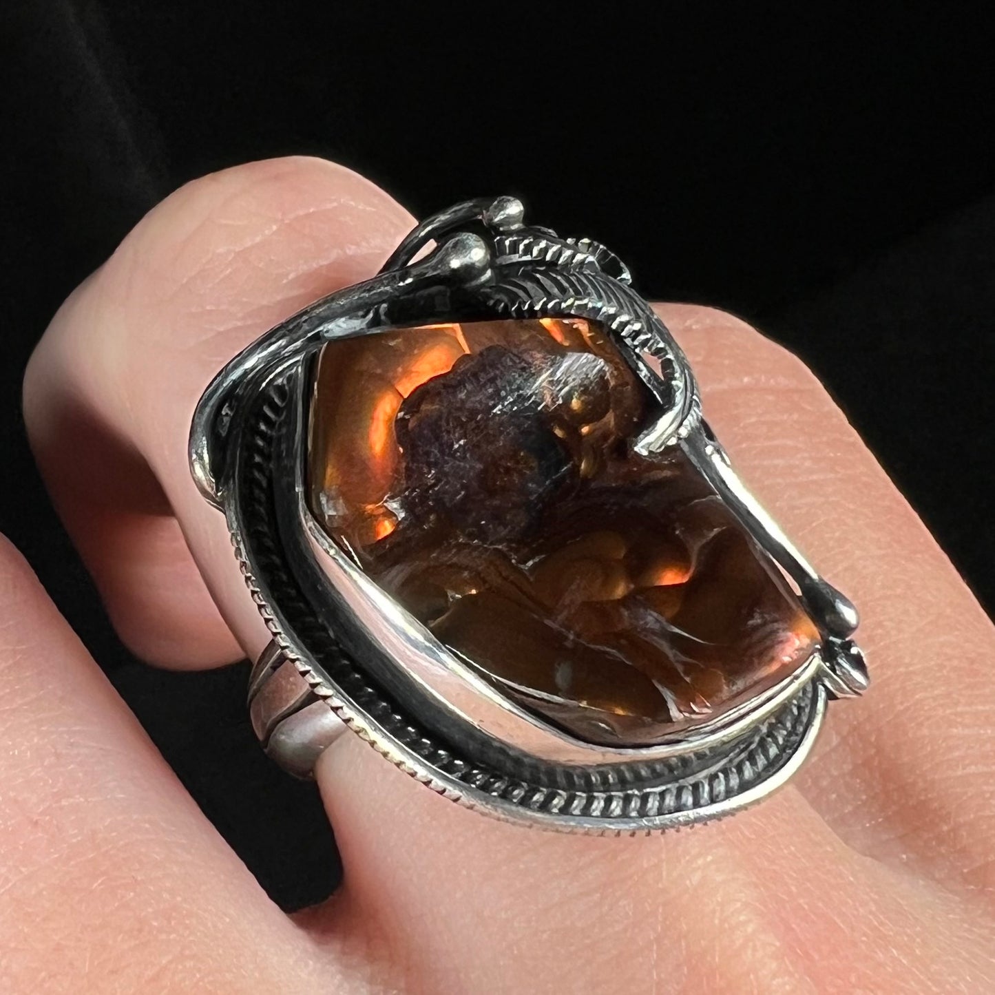 Close-up angled shot of a men's silver, Southwest-style fire agate ring worn on a finger.