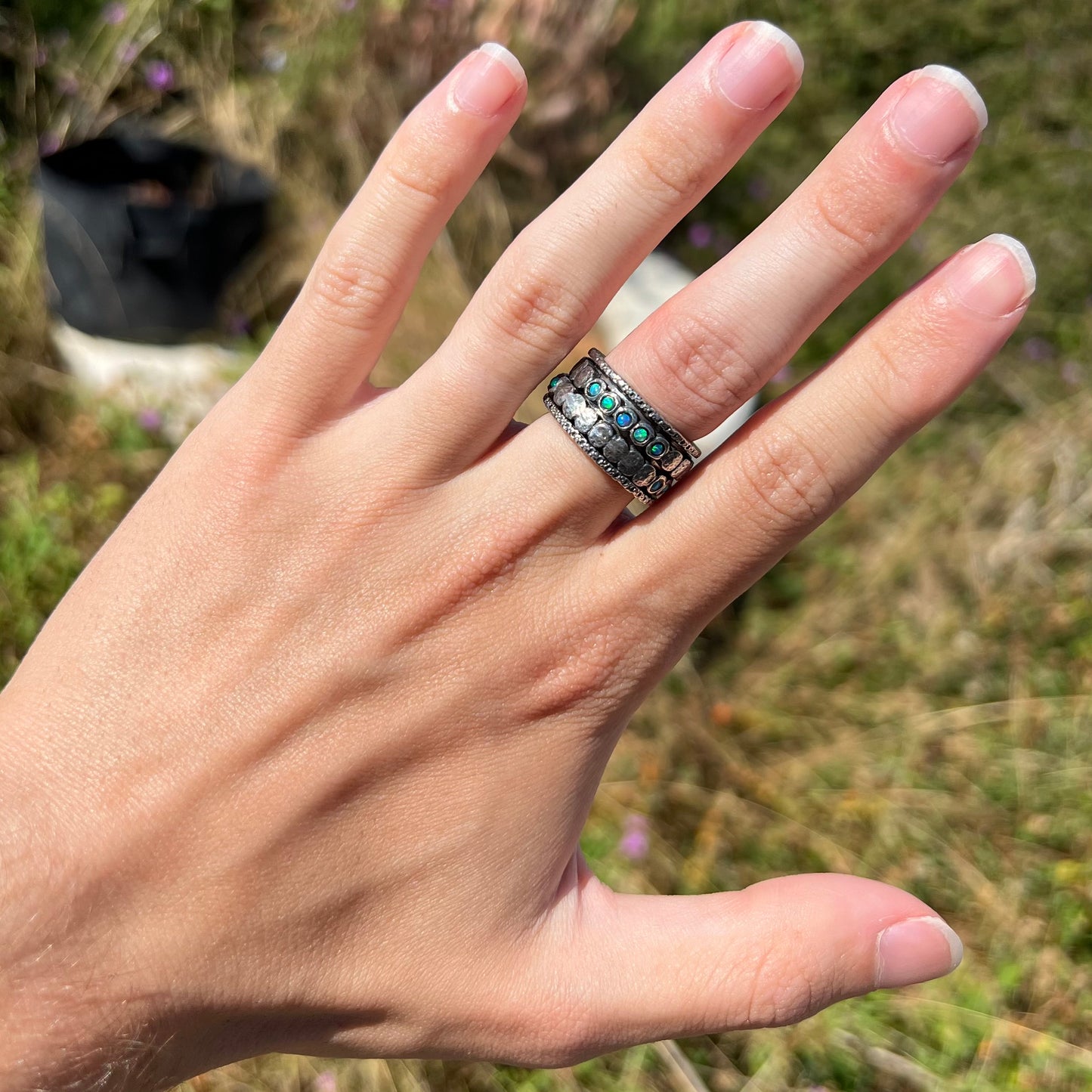 Hand wearing a men's silver opal ring in the sunlight against a blurred outdoor background.