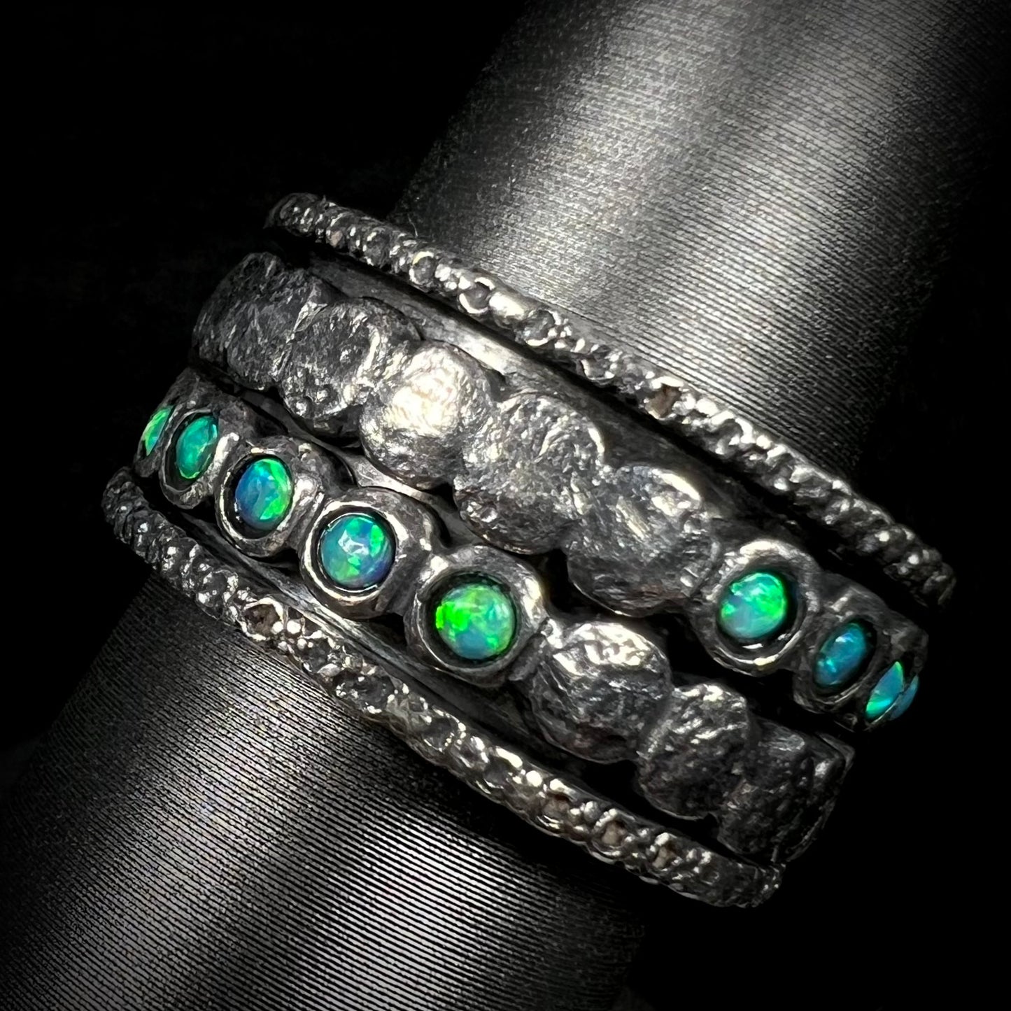 Men's silver opal spinner ring with round, green opals, shown at an angle against a black background.