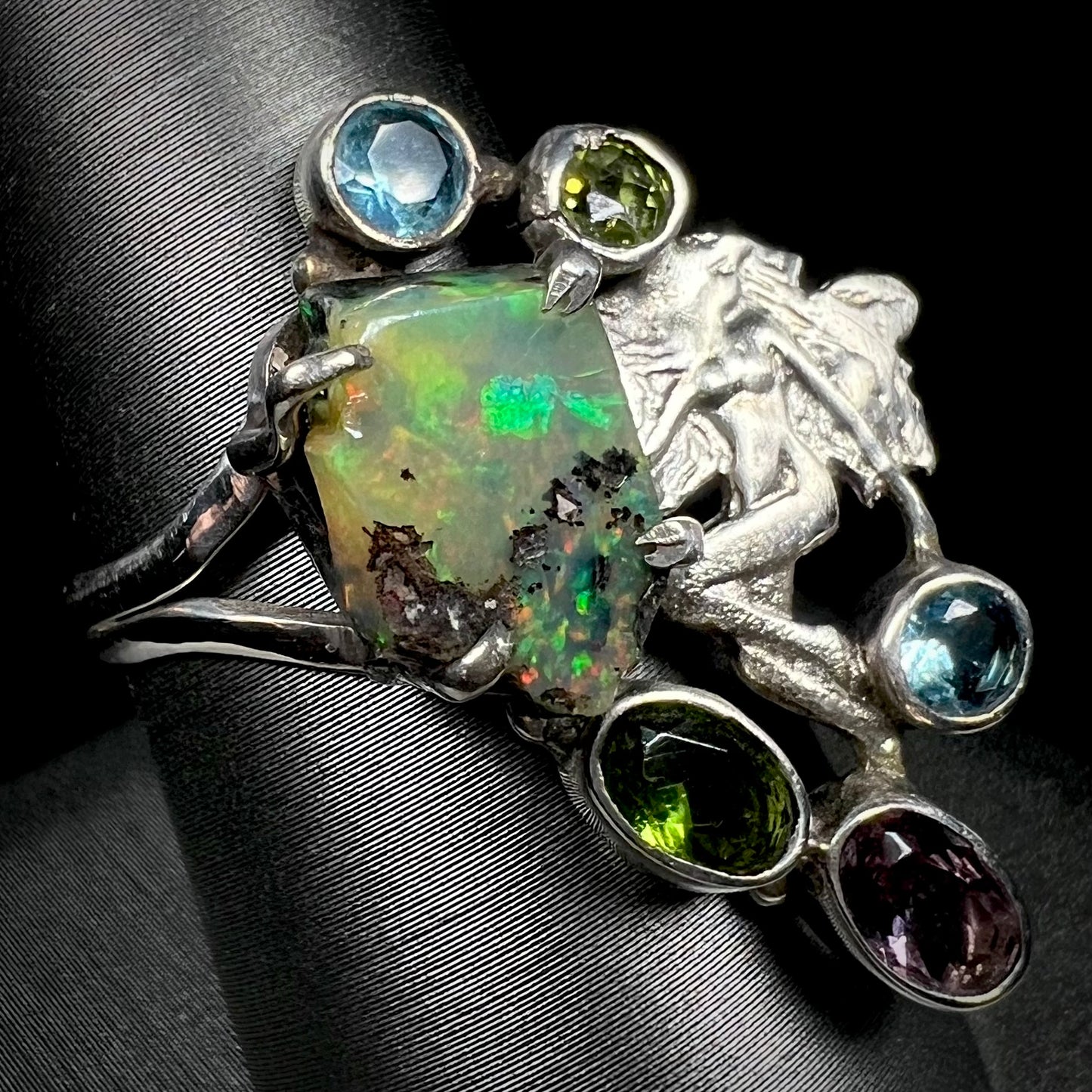 A silver men's ring set with rough Virgin Valley opal and gems with a female figure design shown from an angle.