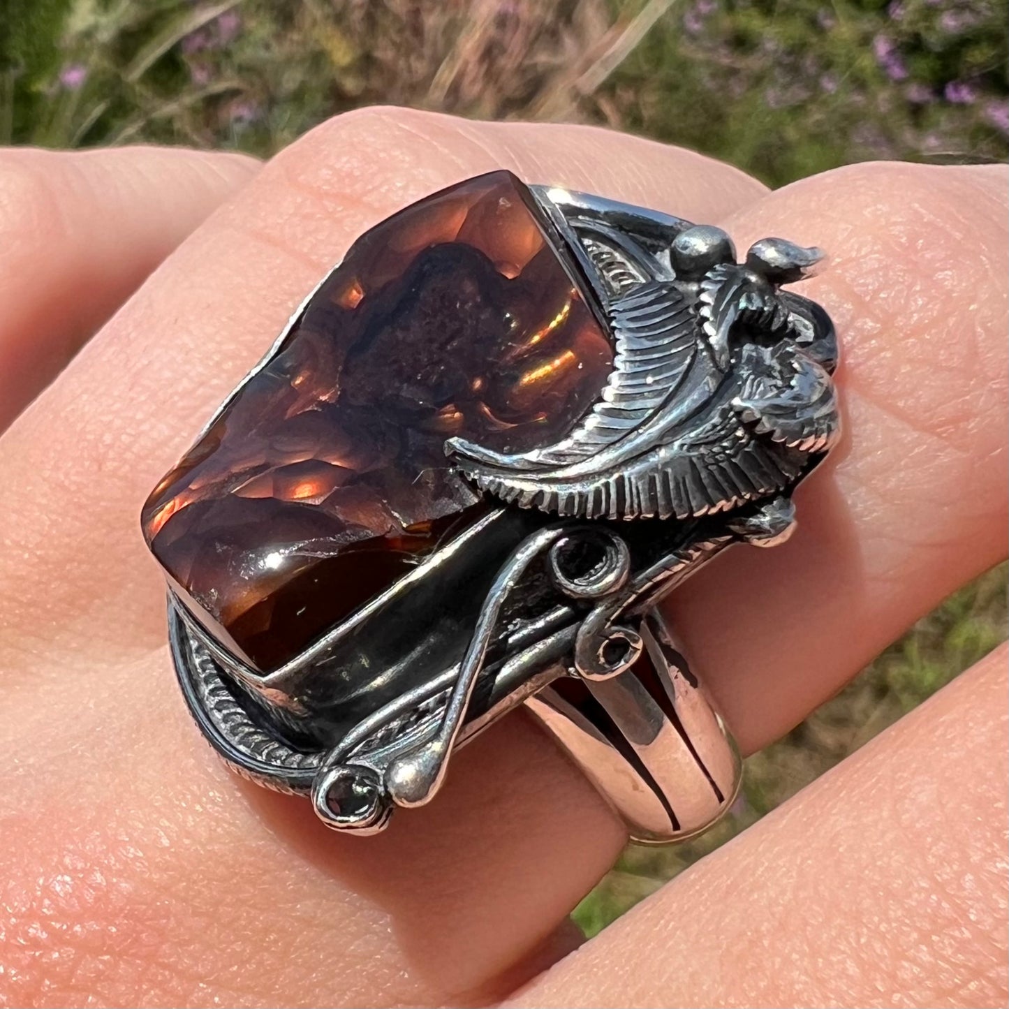 A men's silver, Southwest-style fire agate ring shown from an angled view in the sunlight on a finger.