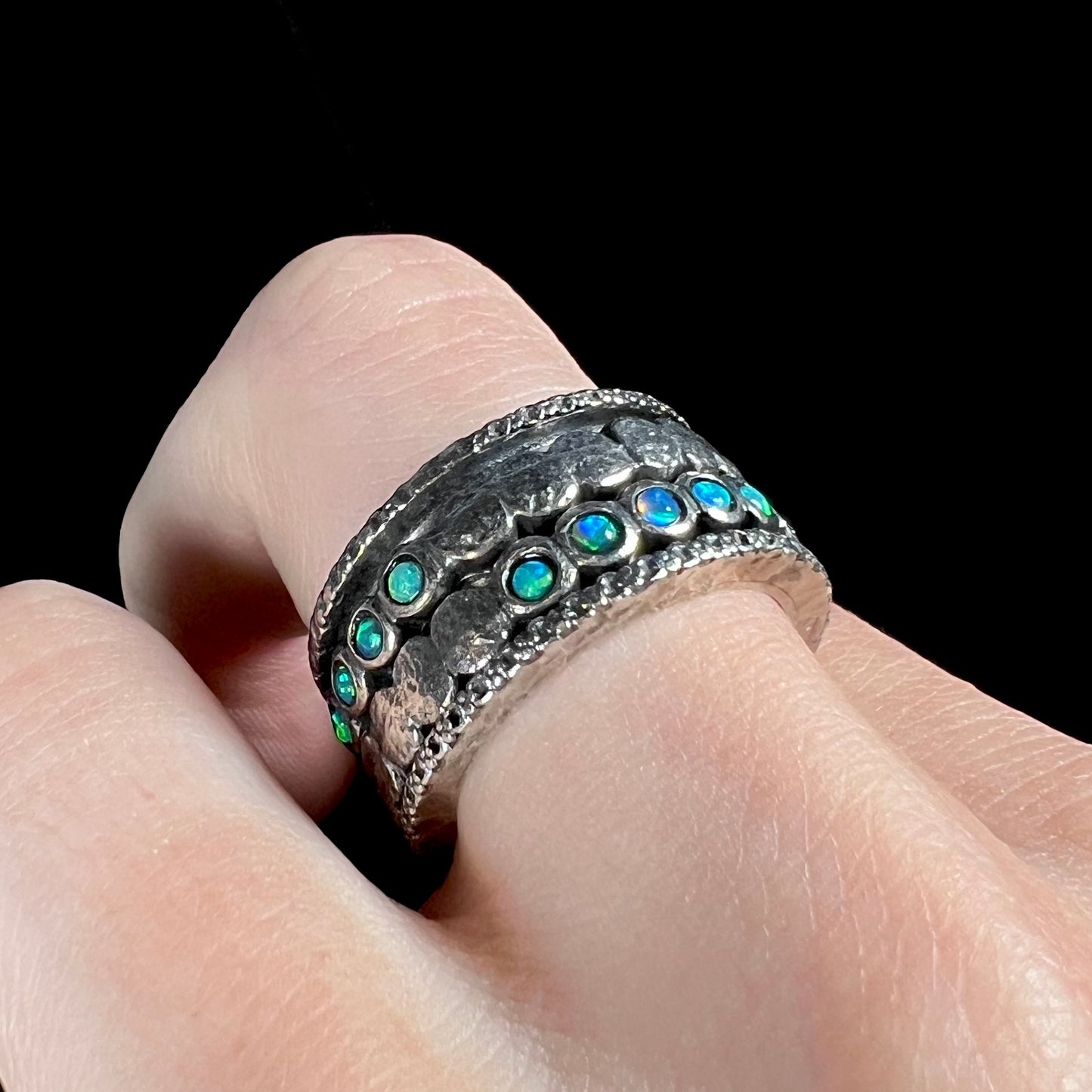 A men's spinner ring set with round opal gemstones in sterling silver, worn on a finger.