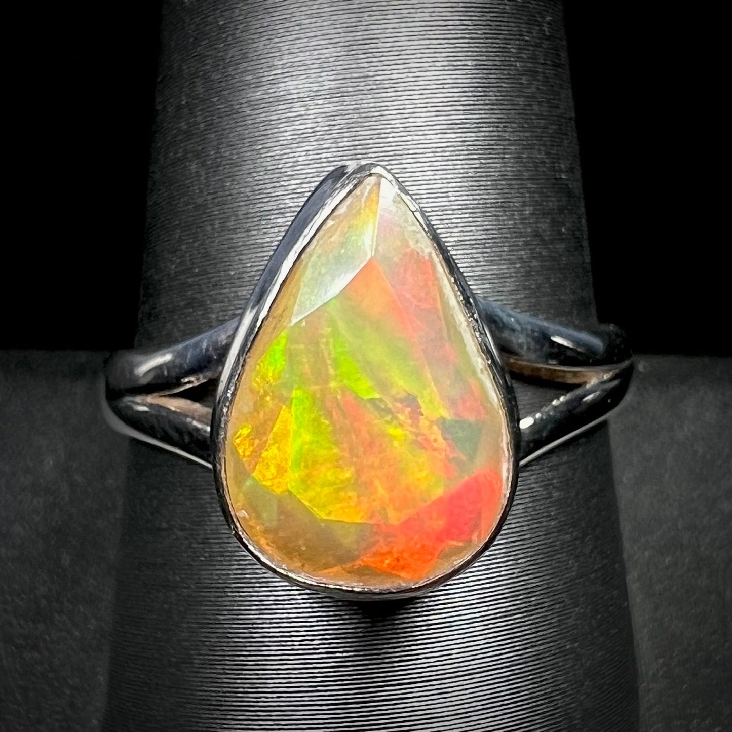 A unisex sterling silver ring set with a faceted pear shaped Ethiopian fire opal. The opal plays orange, red, and green colors.