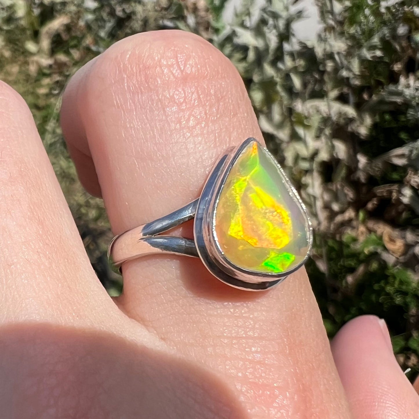 A unisex sterling silver ring set with a faceted pear shaped Ethiopian fire opal. The opal plays orange, red, and green colors.