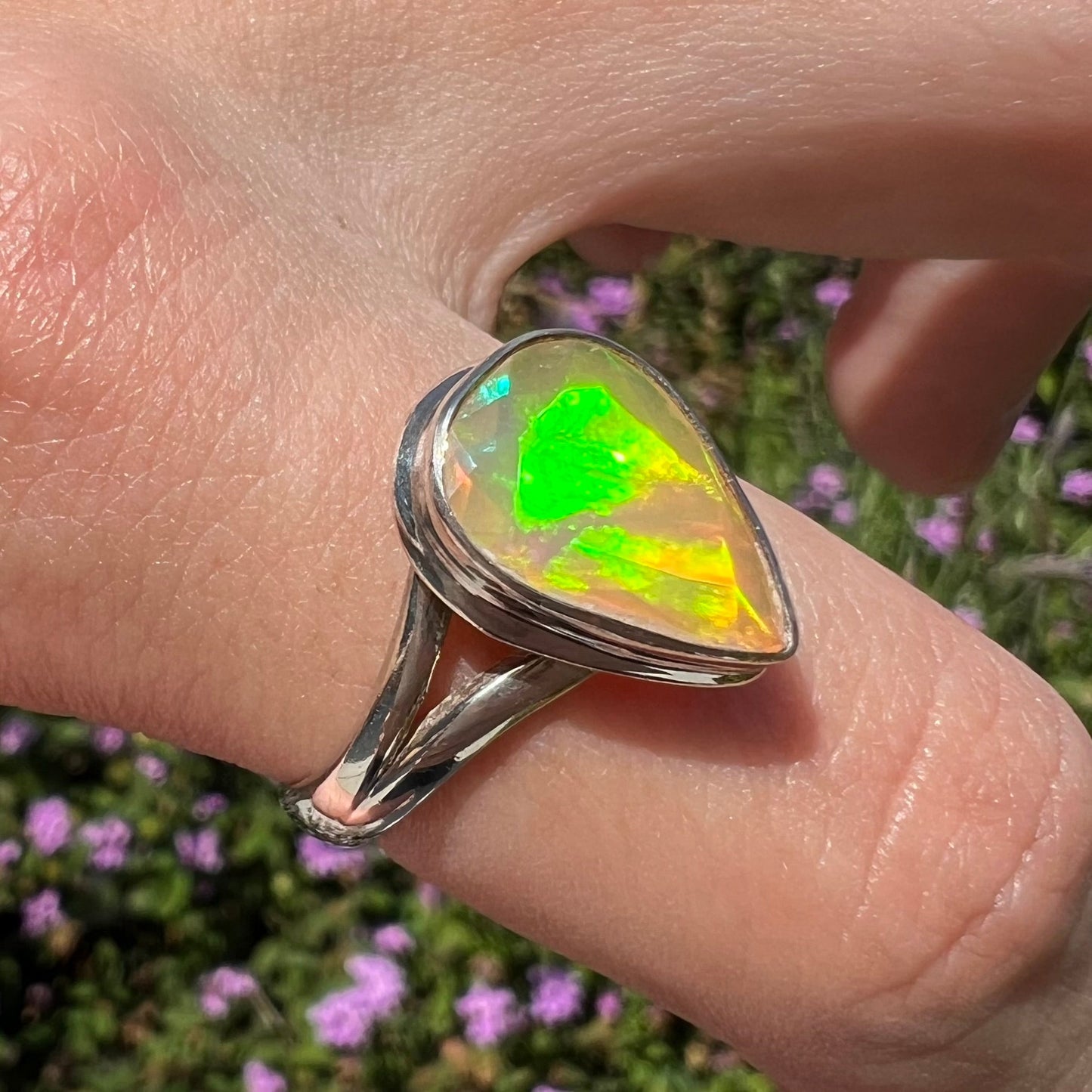 A unisex sterling silver ring set with a faceted pear shaped Ethiopian fire opal. The opal plays orange, red, and green colors.