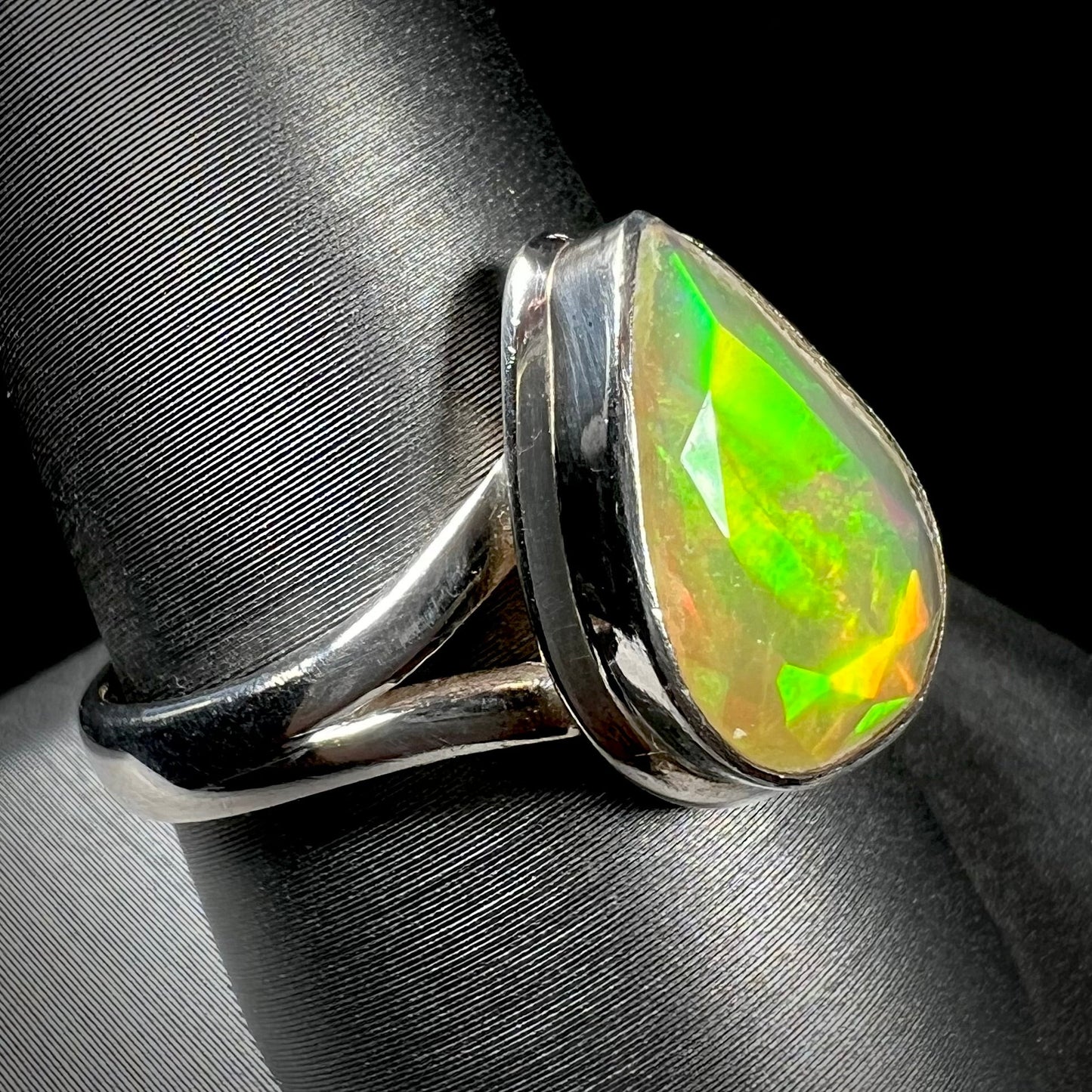 A unisex sterling silver ring set with a faceted pear shaped Ethiopian fire opal. The opal plays orange, red, and green colors.