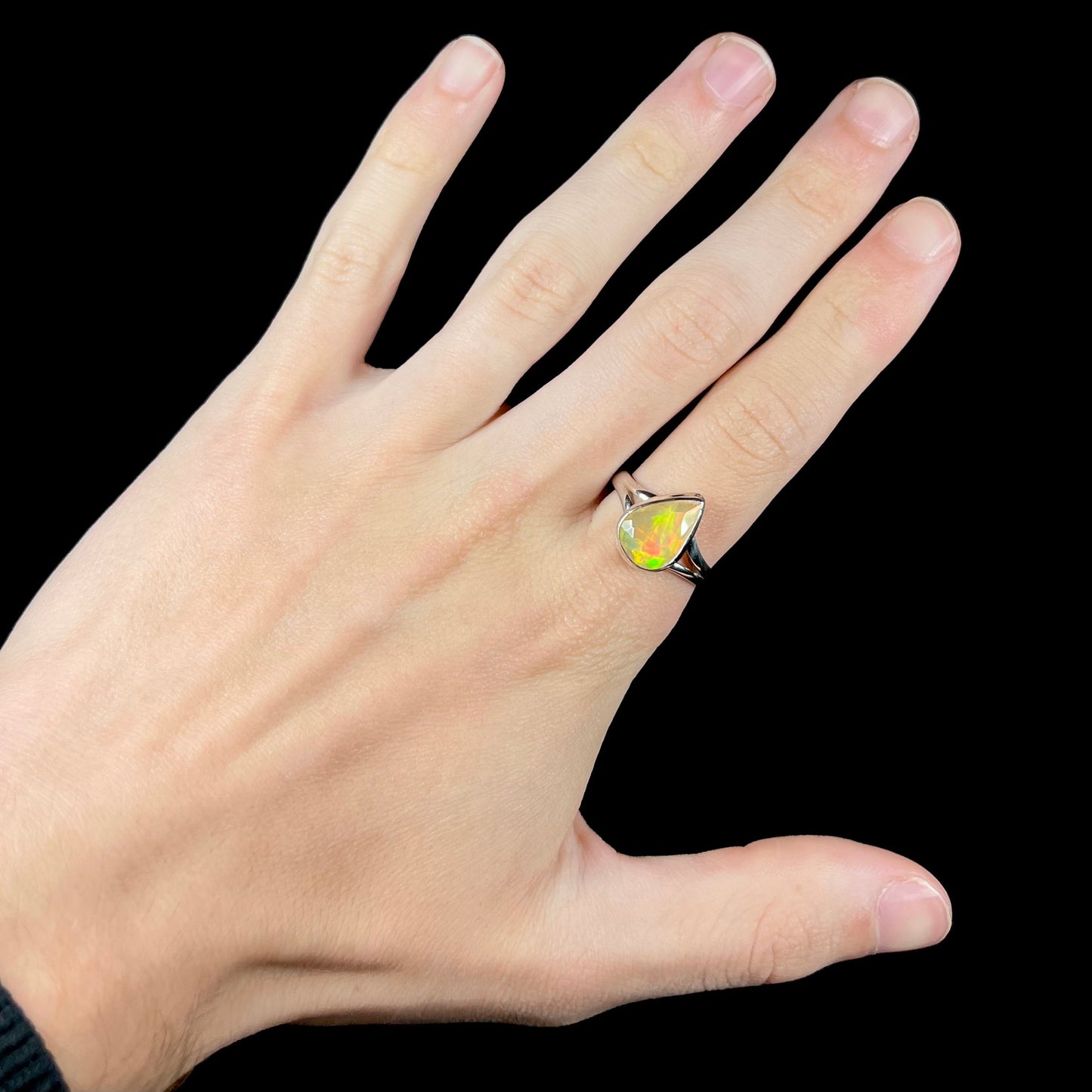 A unisex sterling silver ring set with a faceted pear shaped Ethiopian fire opal. The opal plays orange, red, and green colors.
