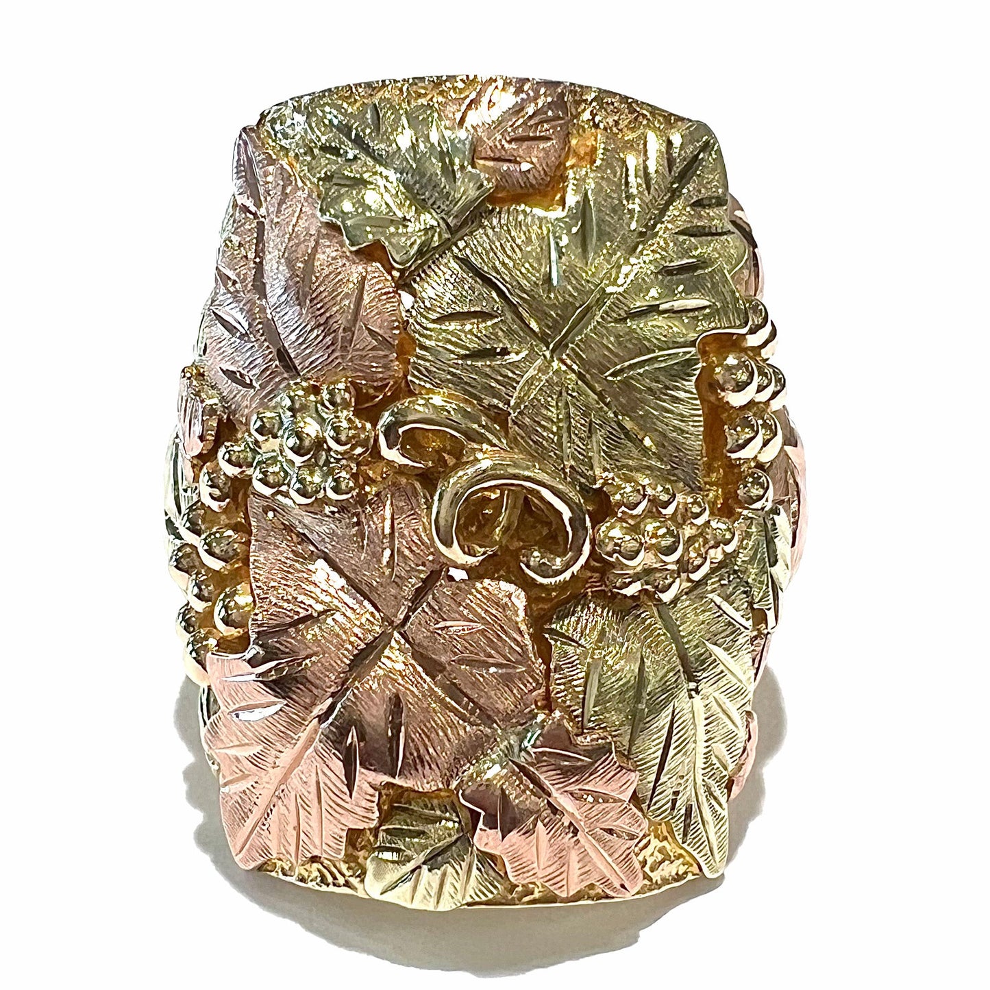 A men's solid gold ring. The ring is Black Hills gold featuring a grapevine and leaf motif with rose and green gold designs.