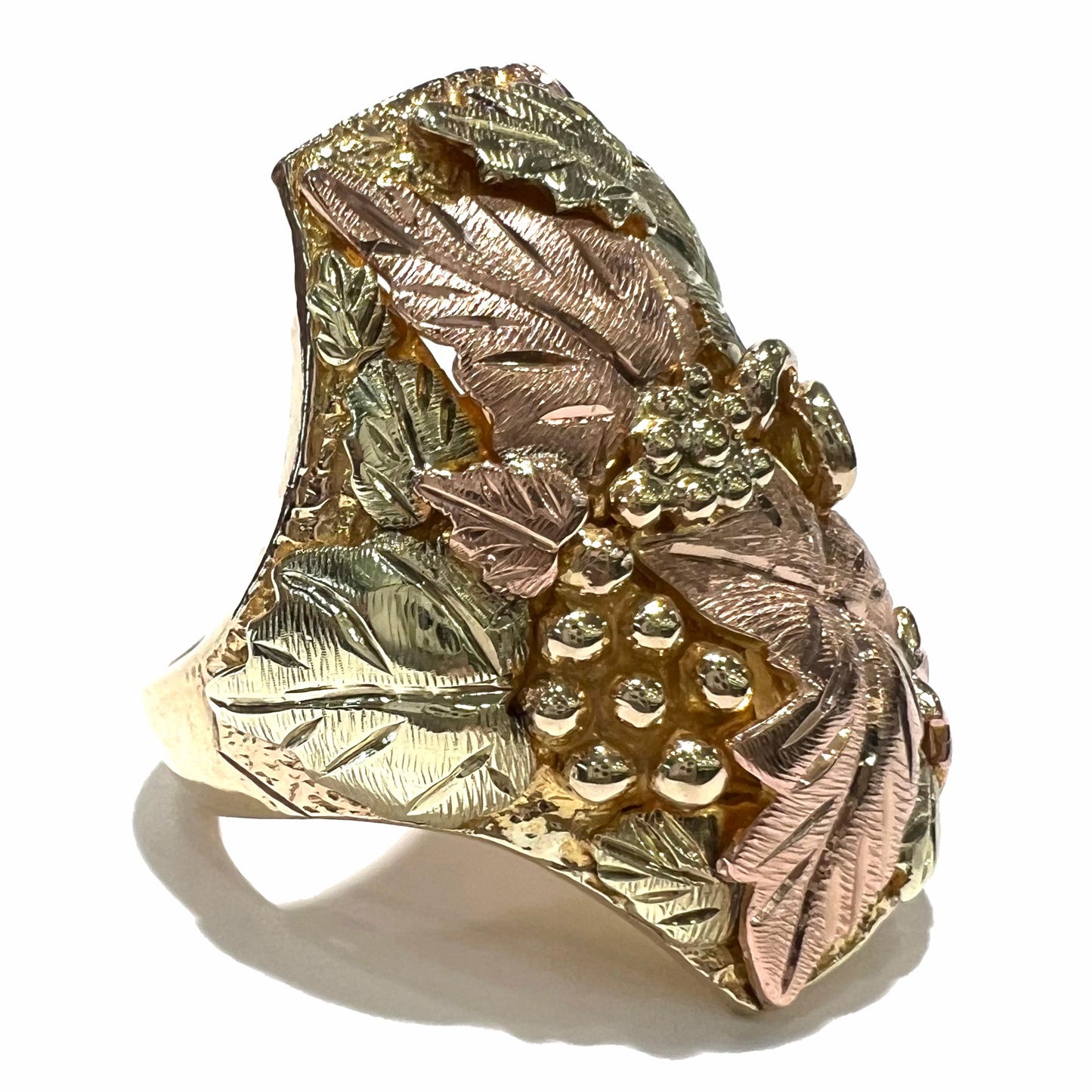 A men's solid gold ring. The ring is Black Hills gold featuring a grapevine and leaf motif with rose and green gold designs.
