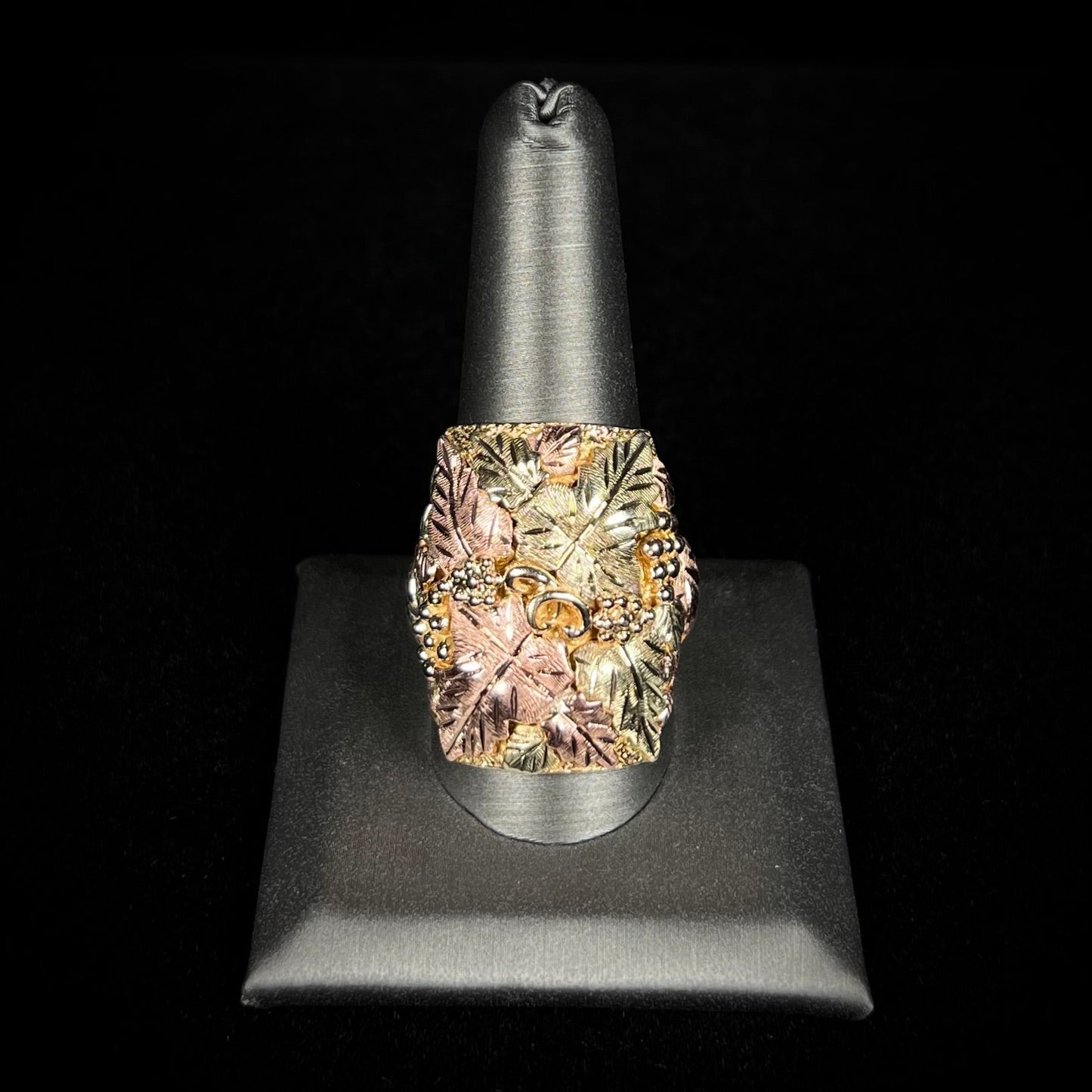A men's solid gold ring. The ring is Black Hills gold featuring a grapevine and leaf motif with rose and green gold designs.