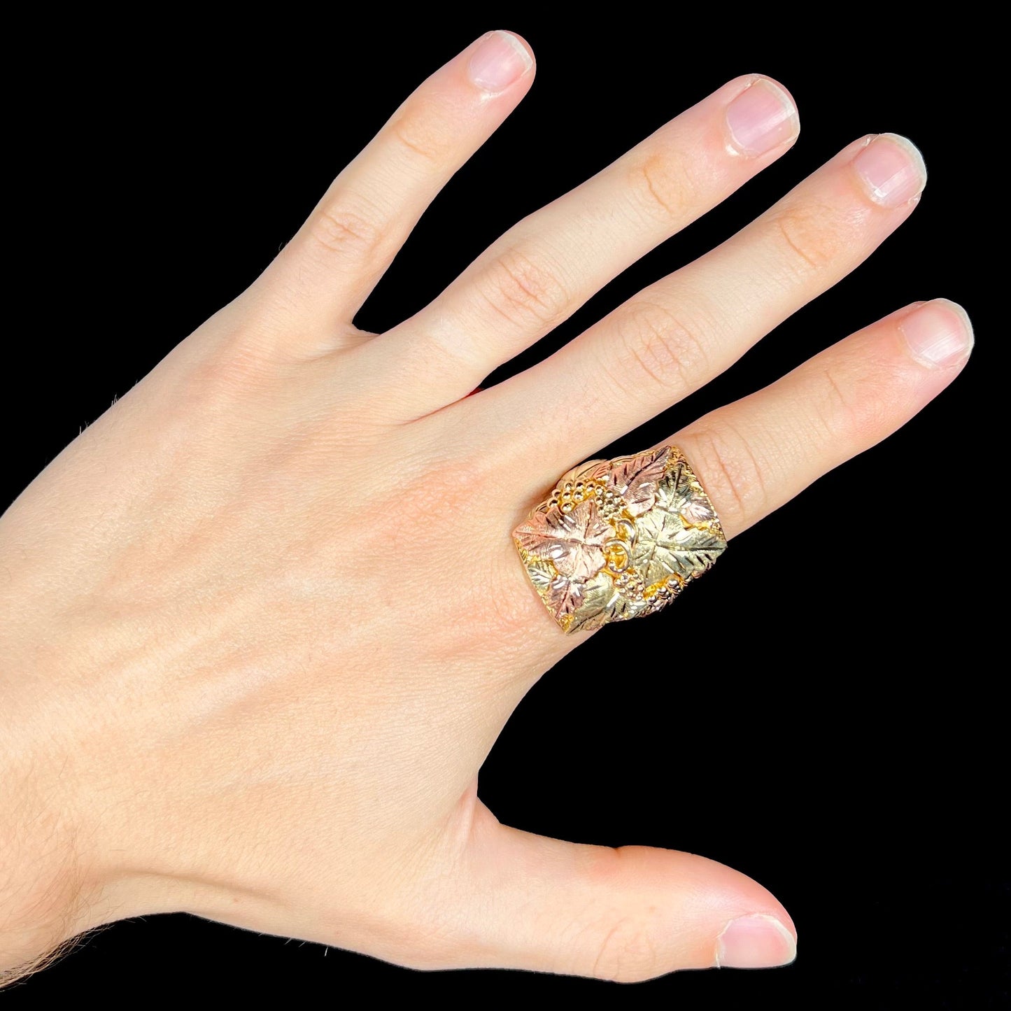A men's solid gold ring. The ring is Black Hills gold featuring a grapevine and leaf motif with rose and green gold designs.