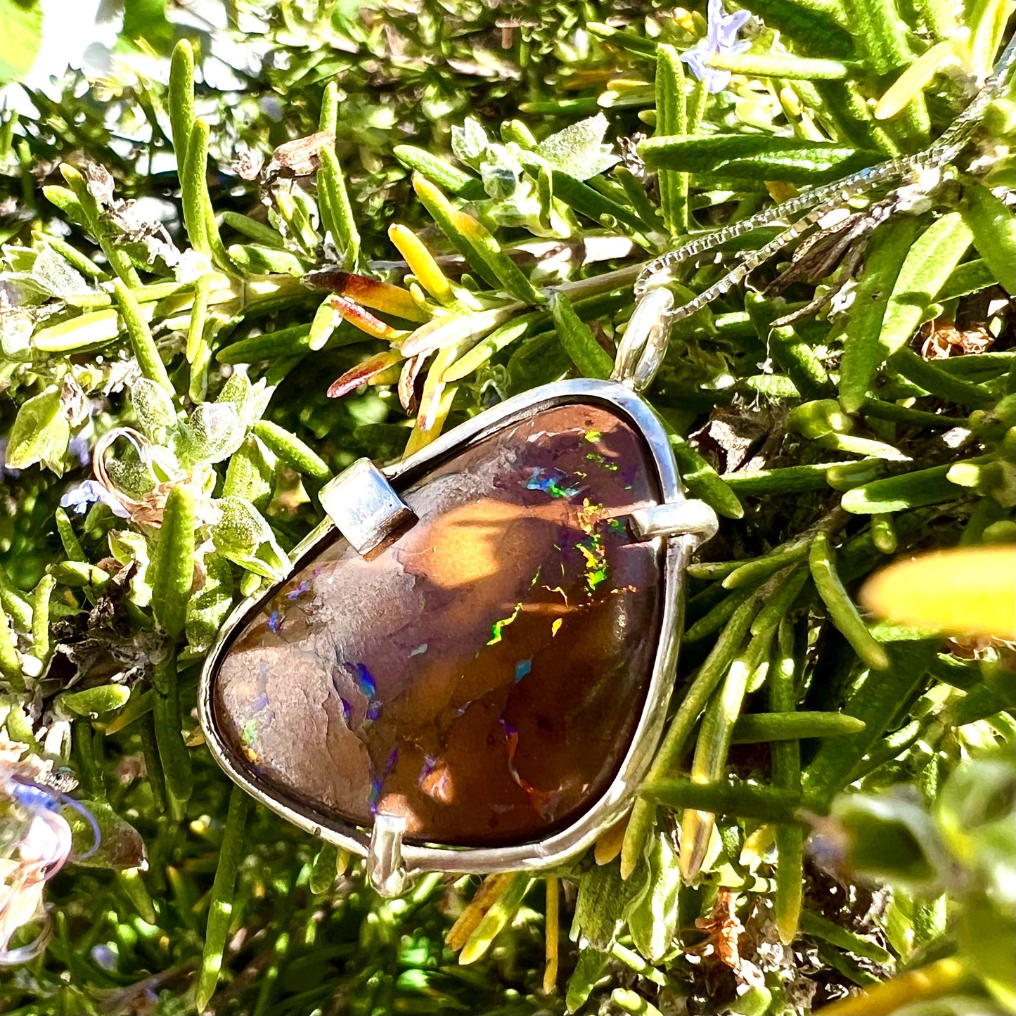 A handmade sterling silver pendant bezel and prong set with a natural boulder opal stone. The opal shines veins of color.
