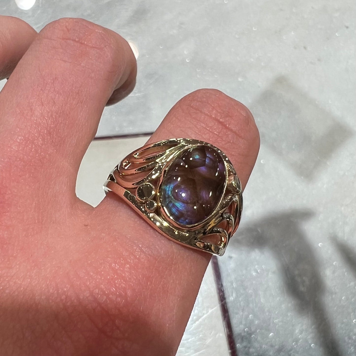 An oval cabochon cut fire agate with purple and blue colors set in a yellow gold men's ring.