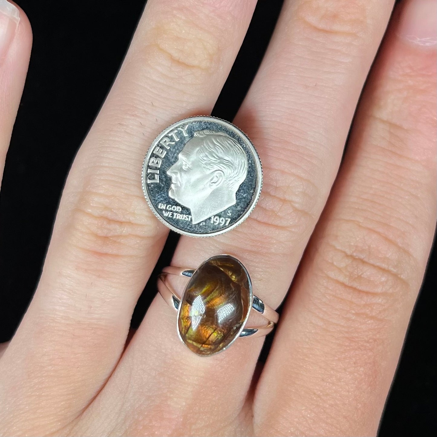 A sterling silver Mexican fire agate ring with a split shank worn on a finger with a dime coin for scale.