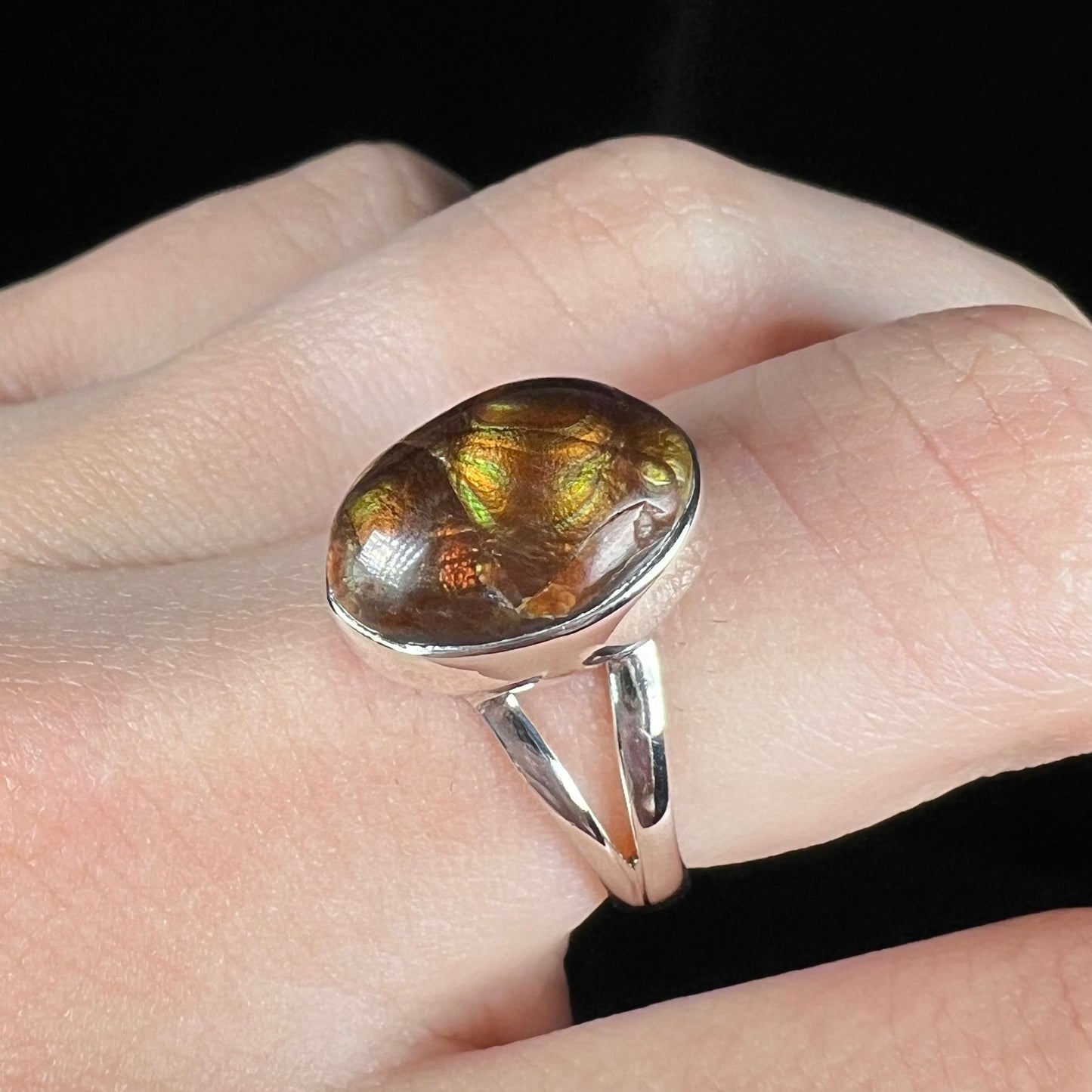 Angled view of a sterling silver Mexican fire agate ring with a split shank, worn on a finger.
