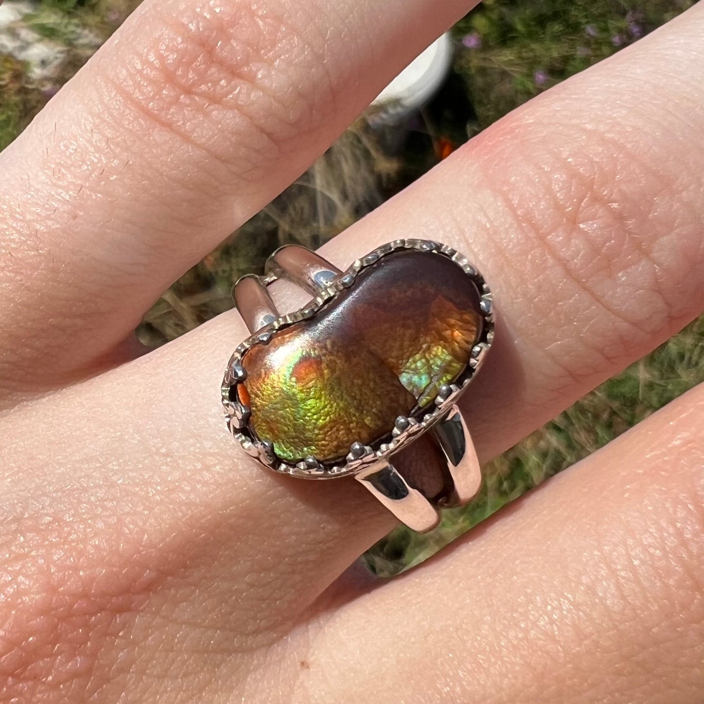 Close-up front view of finger wearing a Mexican fire agate ring with green iridescence in the sunlight.