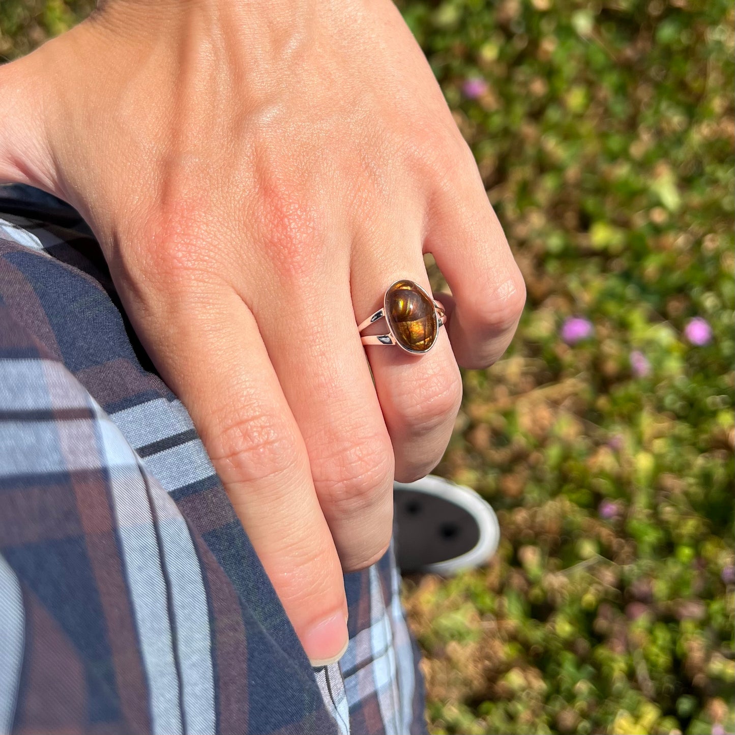 A sterling silver Mexican fire agate ring with a split shank in the sunlight, worn on a hand resting on the model's hip.