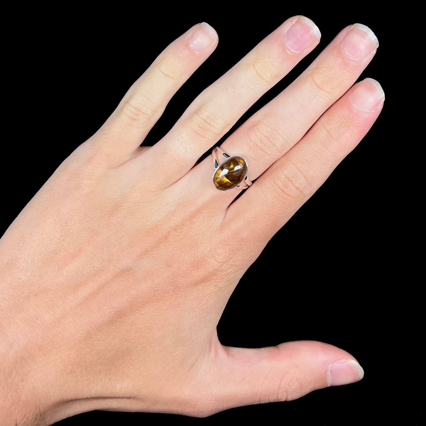 A sterling silver Mexican fire agate ring with a split shank worn on a hand against black background.