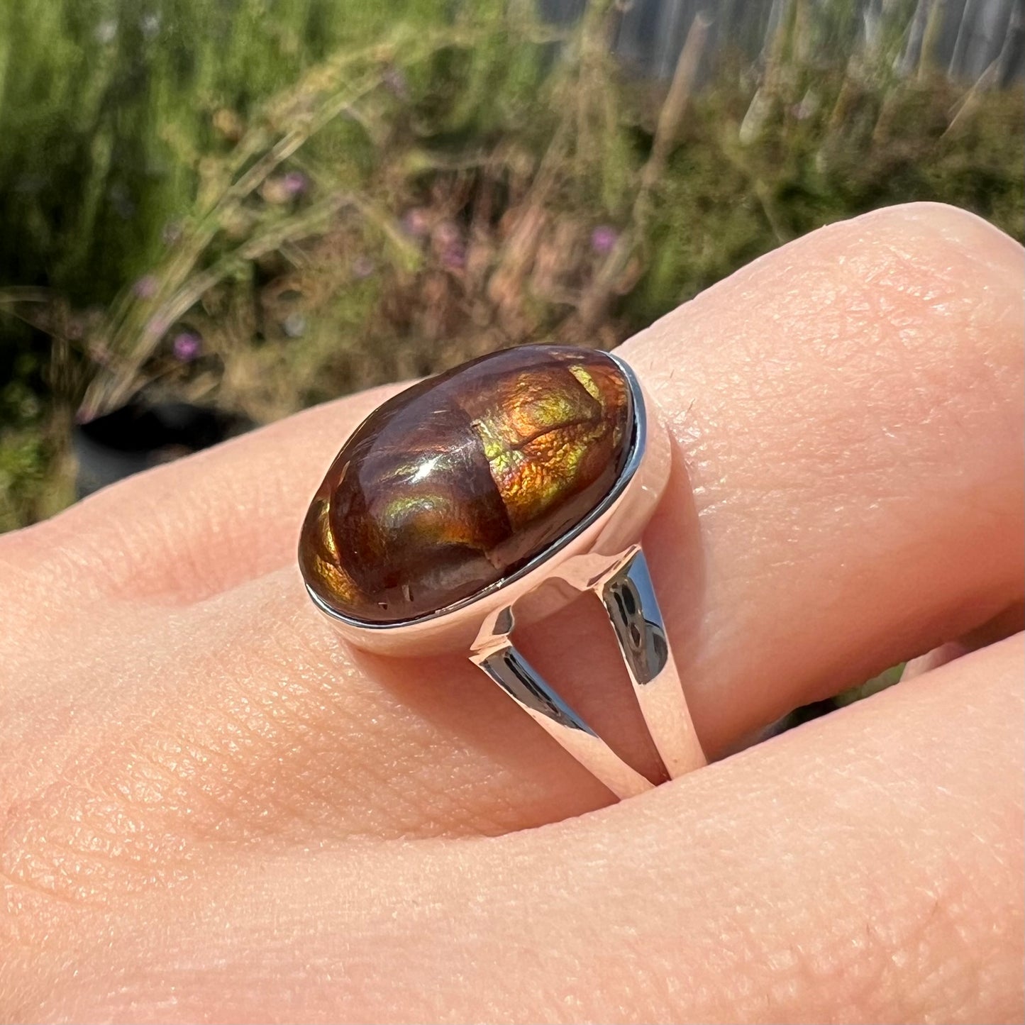 Close-up angled view of a sterling silver Mexican fire agate ring with a split shank worn on a finger.