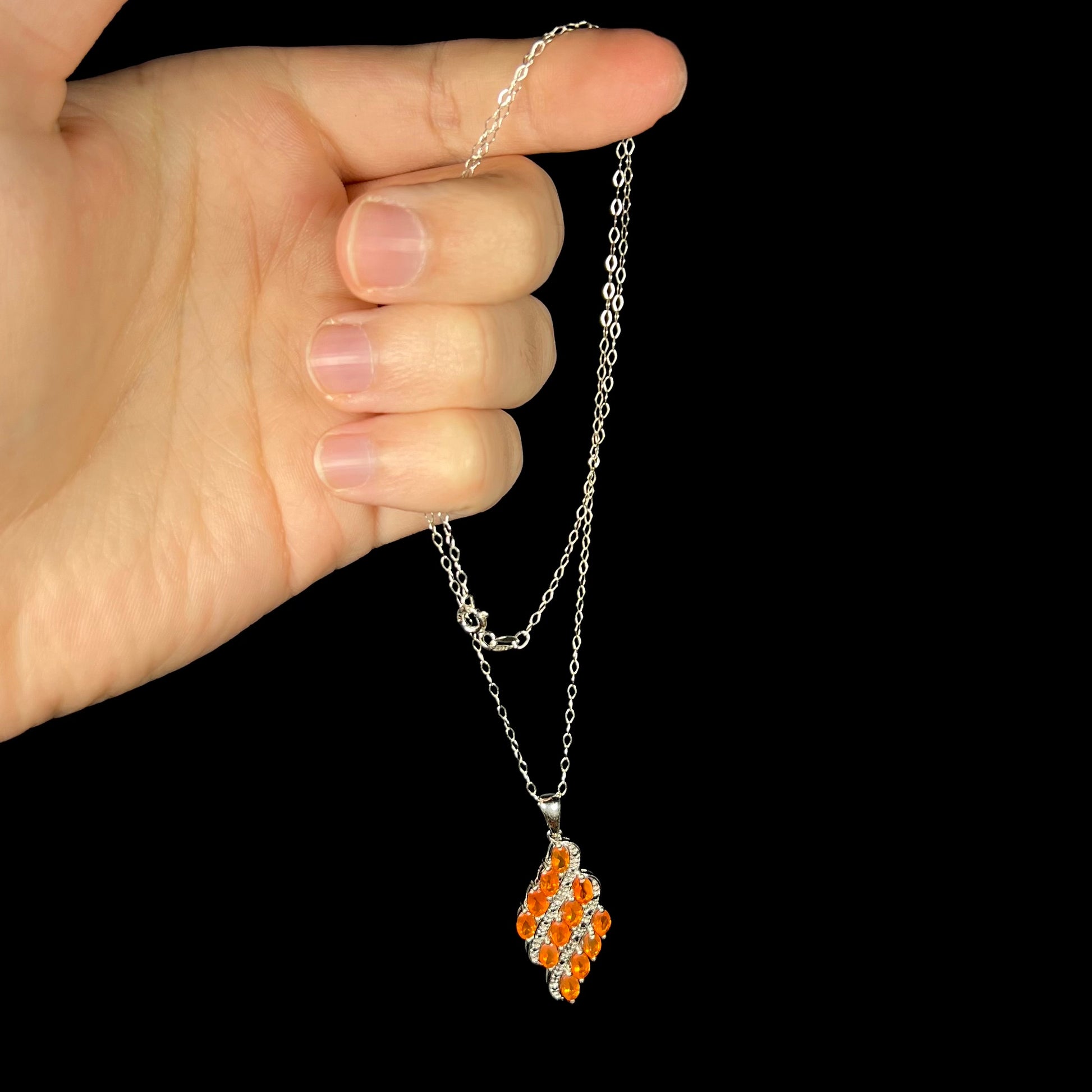 A Mexican fire opal cluster necklace, held from a hand by the chain against a black background.