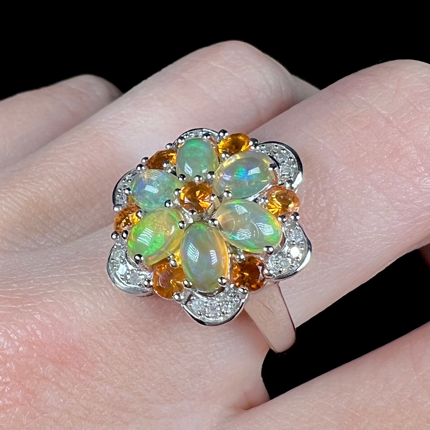 A Mexican fire opal and diamond cluster ring that resembles a flower, worn on a finger and shown at an angle.