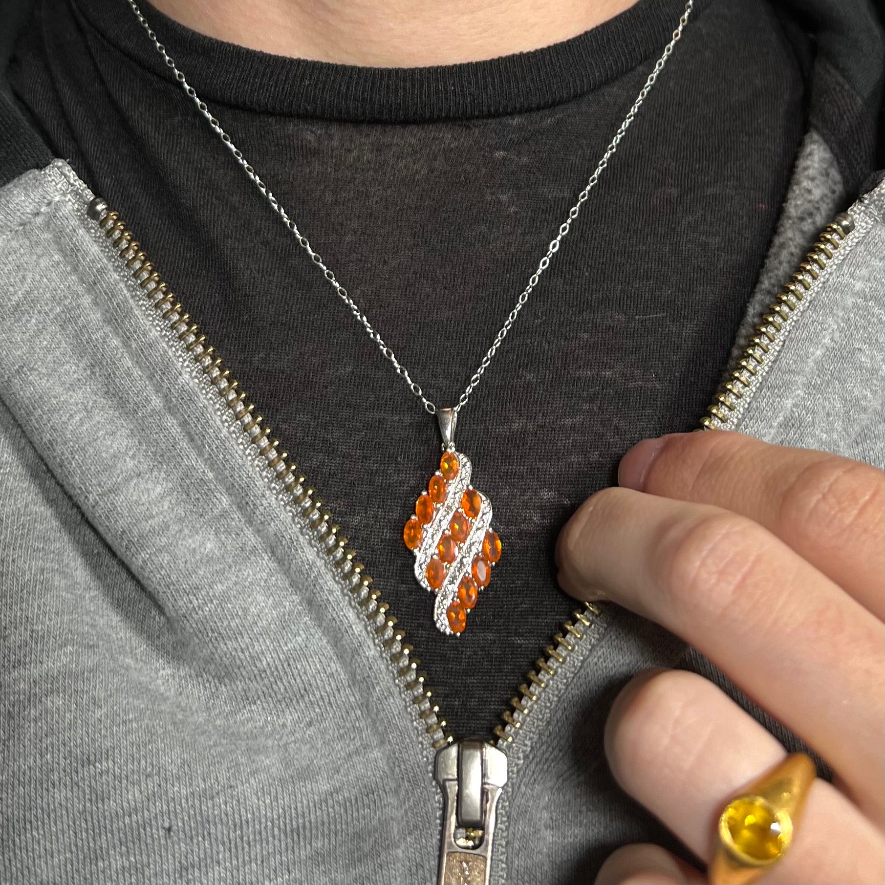 A silver Mexican fire opal necklace, worn around a neck against a dark shirt and partially unzipped hoodie.