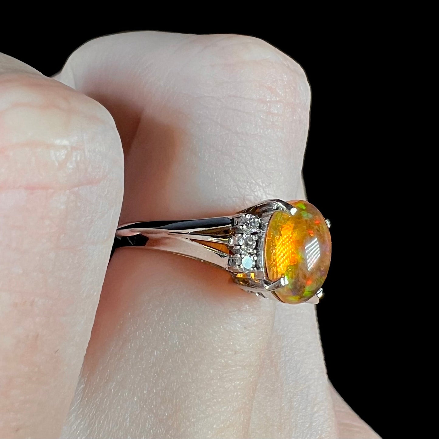 A platinum filigree and diamond-accented Mexican fire opal ring. The opal is orange with green fire.