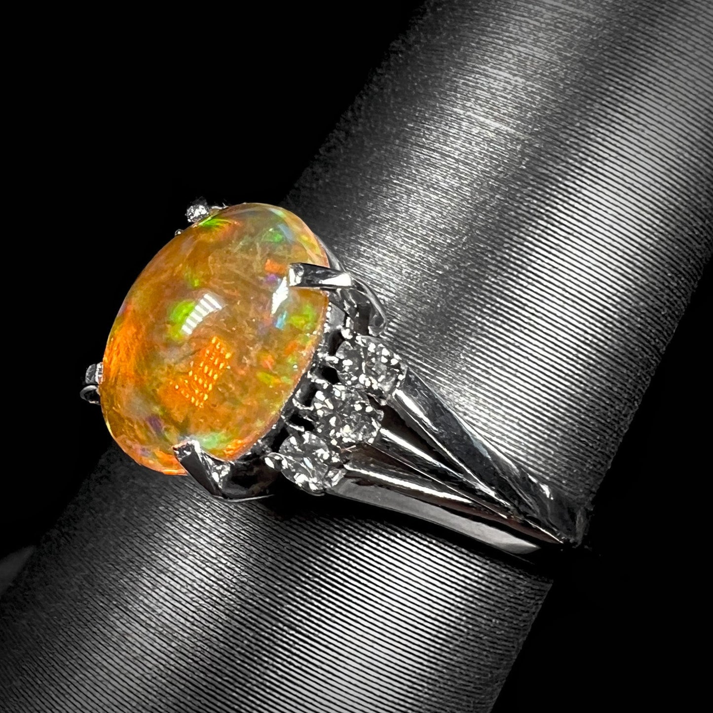 A platinum filigree and diamond-accented Mexican fire opal ring. The opal is orange with green fire.