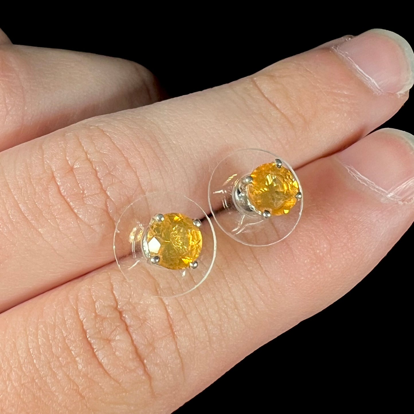 A pair of Mexican fire opal stud earrings in sterling silver held between two fingers at an angle.
