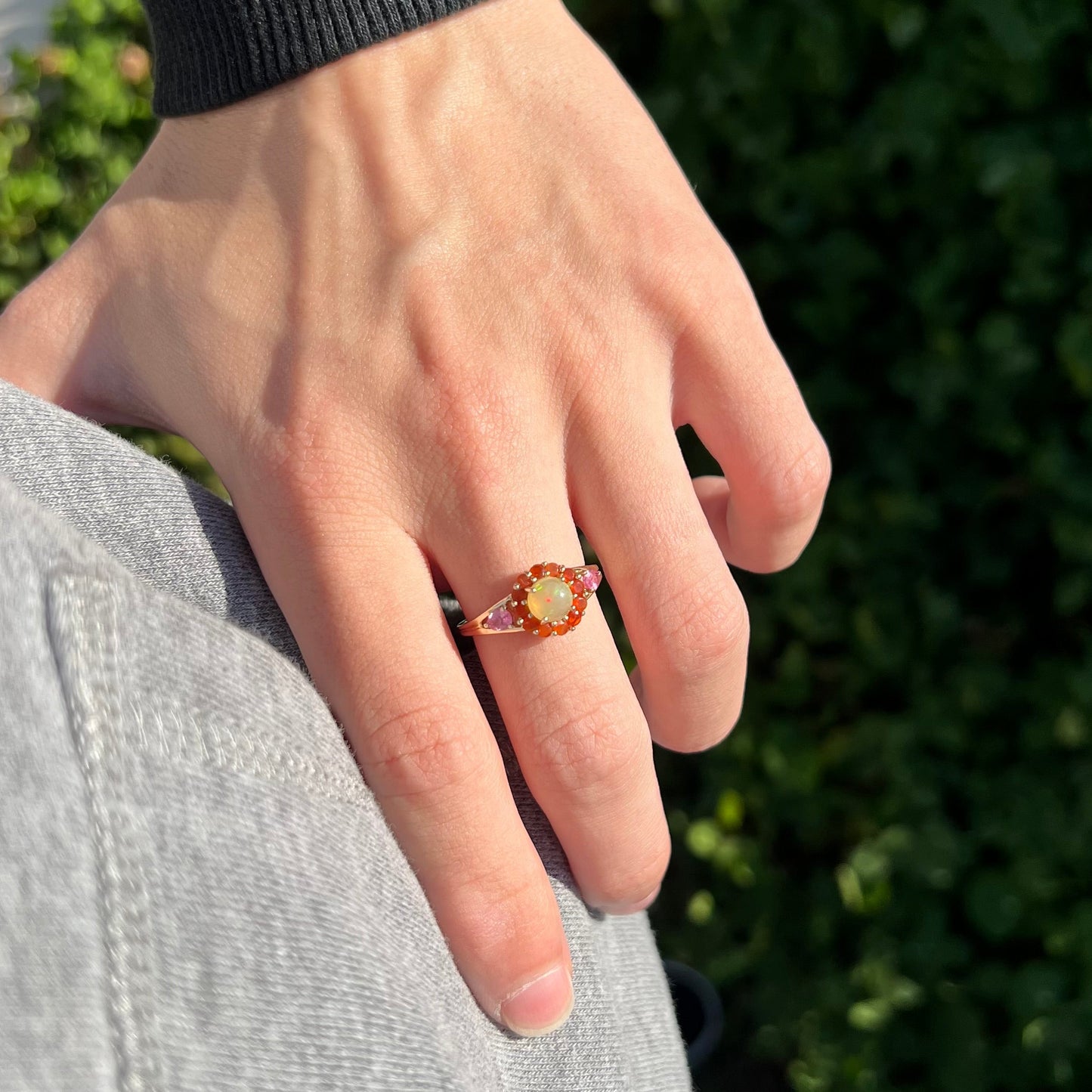 A yellow gold ring mounted with a round Ethiopian opal in a halo of faceted Mexican fire opals. Two pear shaped pink tourmalines accent the sides of the ring.