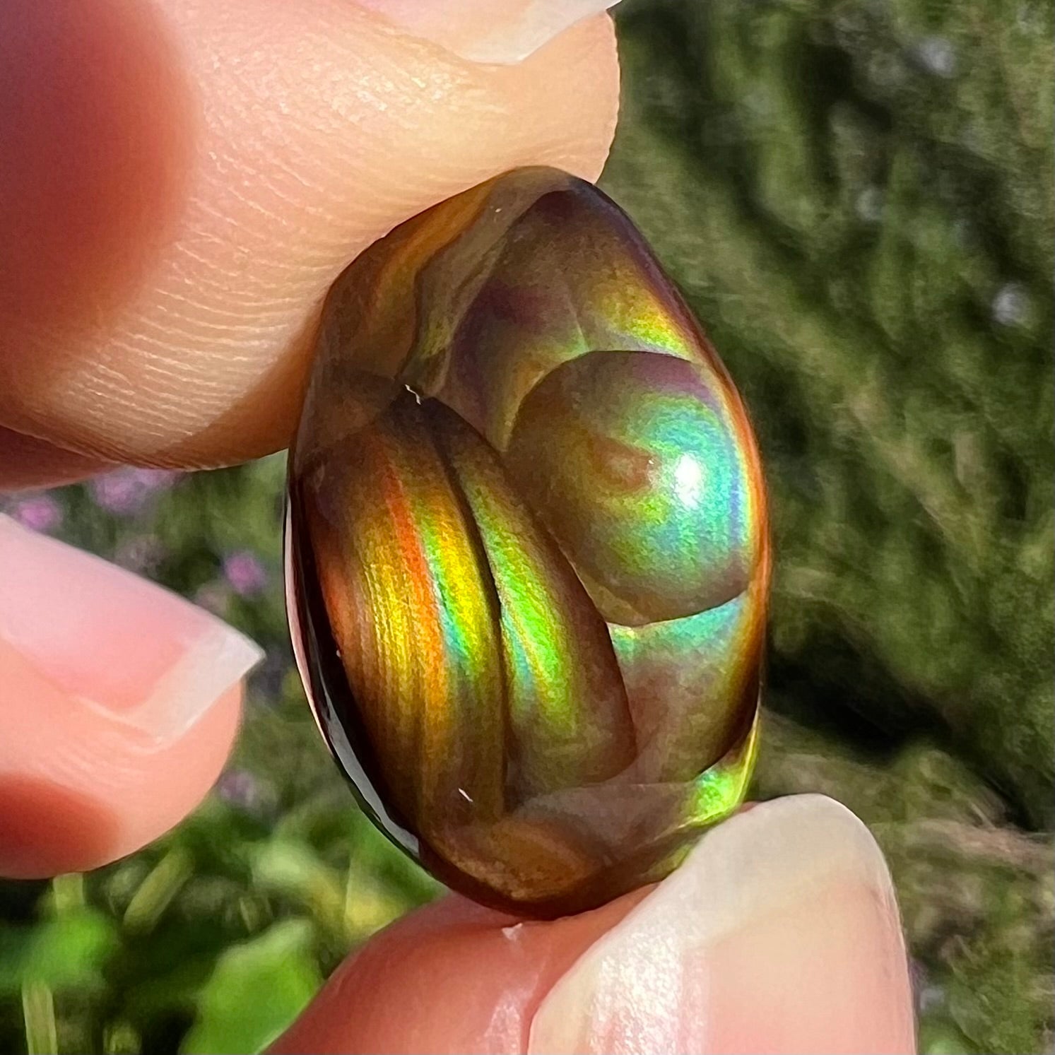 An oval cabochon cut Mexican fire agate stone.  The stone has bright, multicolored iridescent banding.