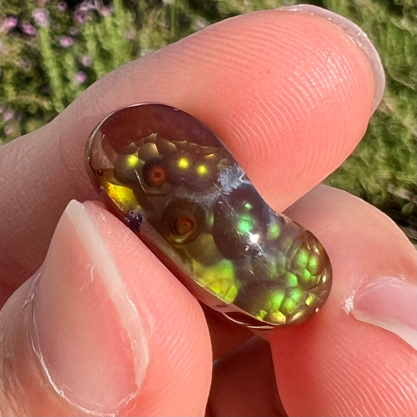 A loose, cabochon cut fire agate gemstone. The stone resembles a foot with a green heel and yellow toes.