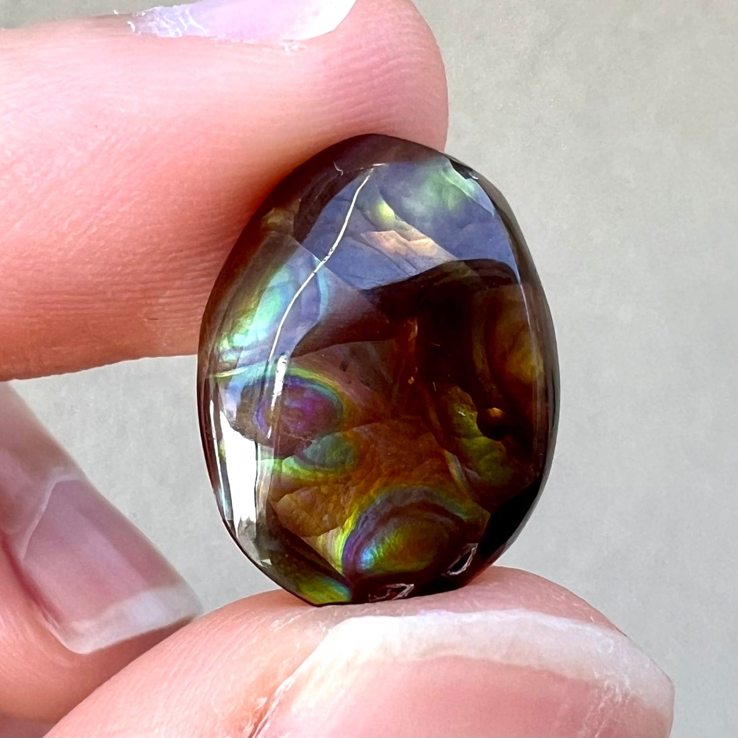 A loose, oval cabochon cut Mexican fire agate stone with pink, orange, and purple banding.