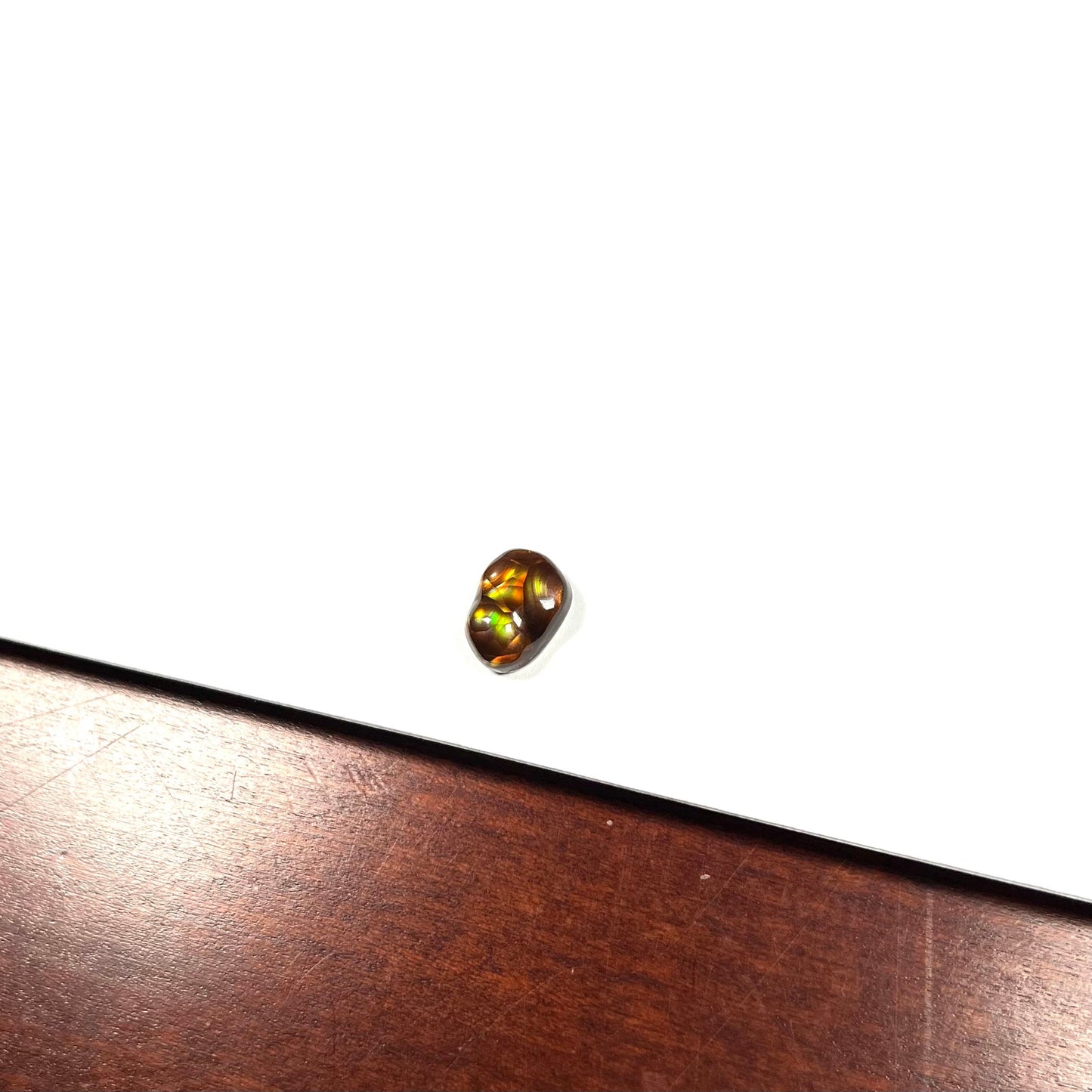 A loose, freefrom cabochon cut Mexican fire agate stone. The stone has red, green, yellow, and purple banding.