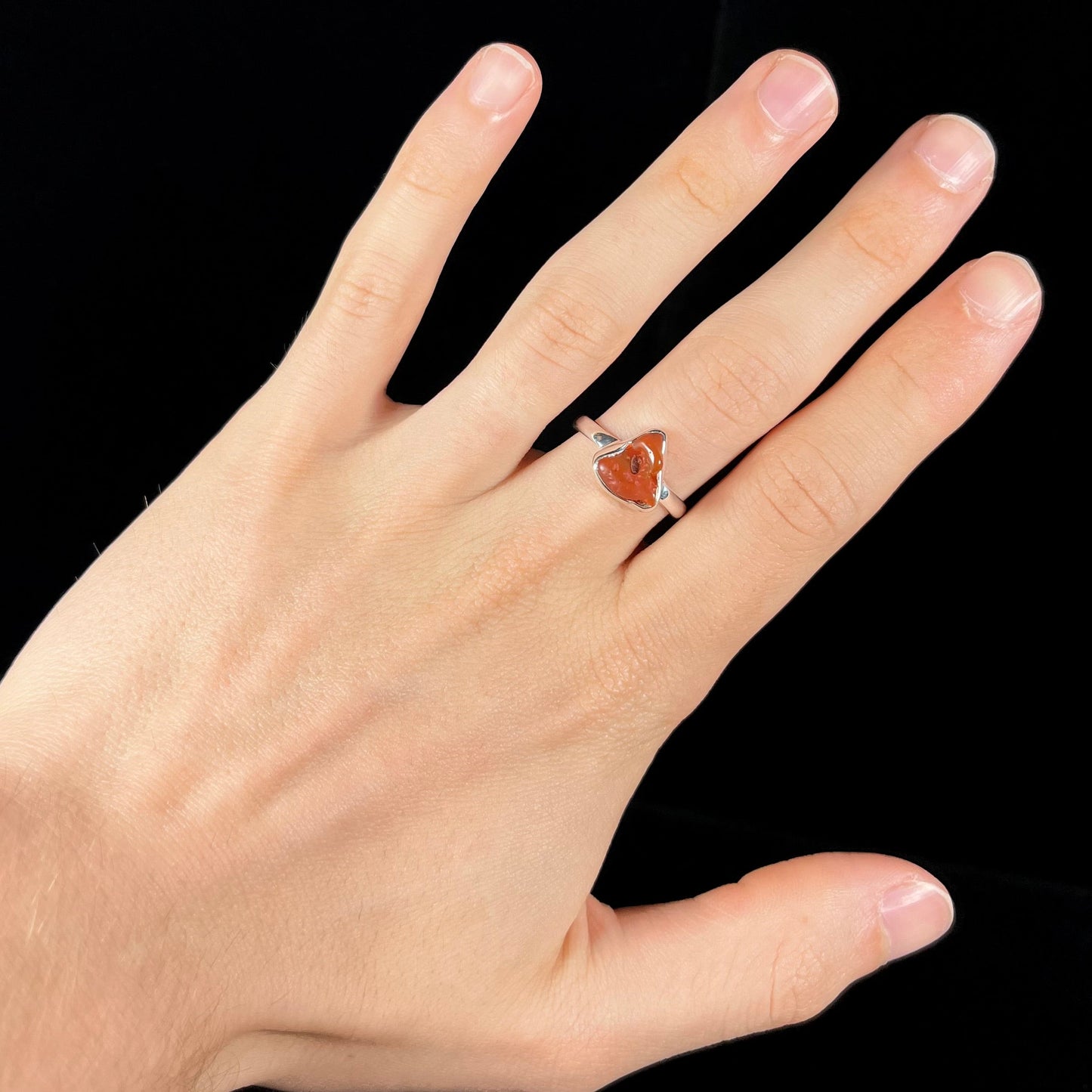 A polished fire opal crystal bezel set into a sterling silver ring. The opal is an orange color.