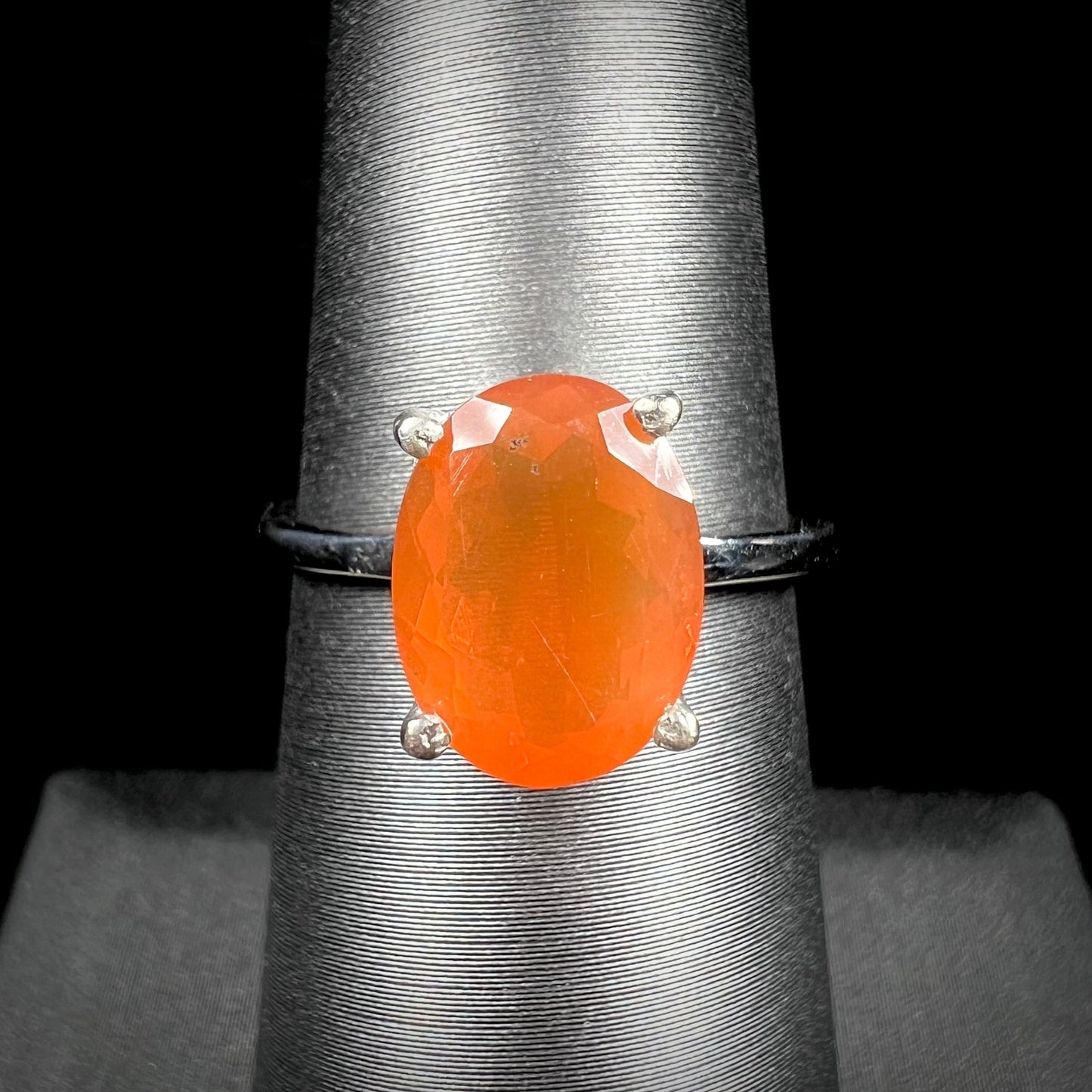 A silver solitaire ring set with a natural, faceted oval cut Mexican fire opal. The stone is a bright orange color.