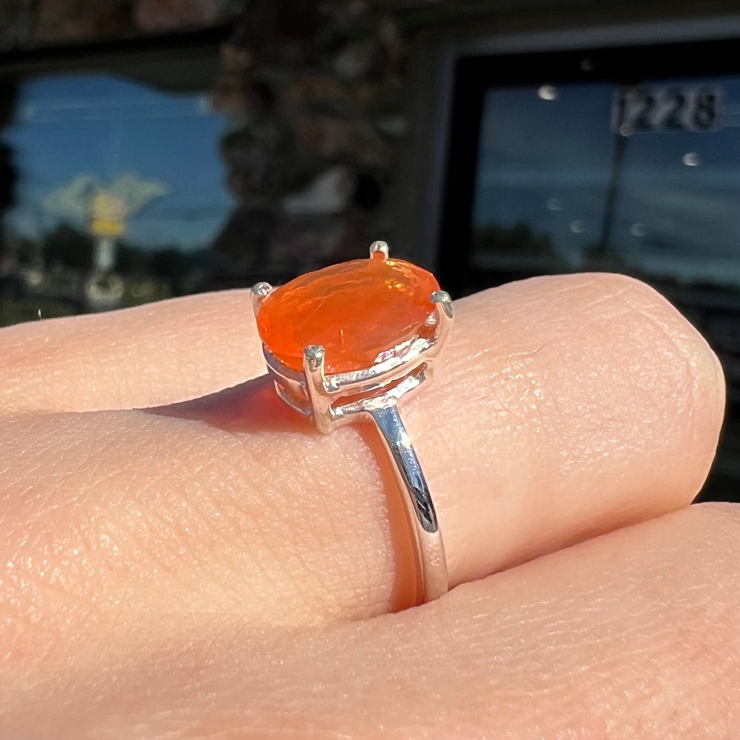 A silver solitaire ring set with a natural, faceted oval cut Mexican fire opal. The stone is a bright orange color.